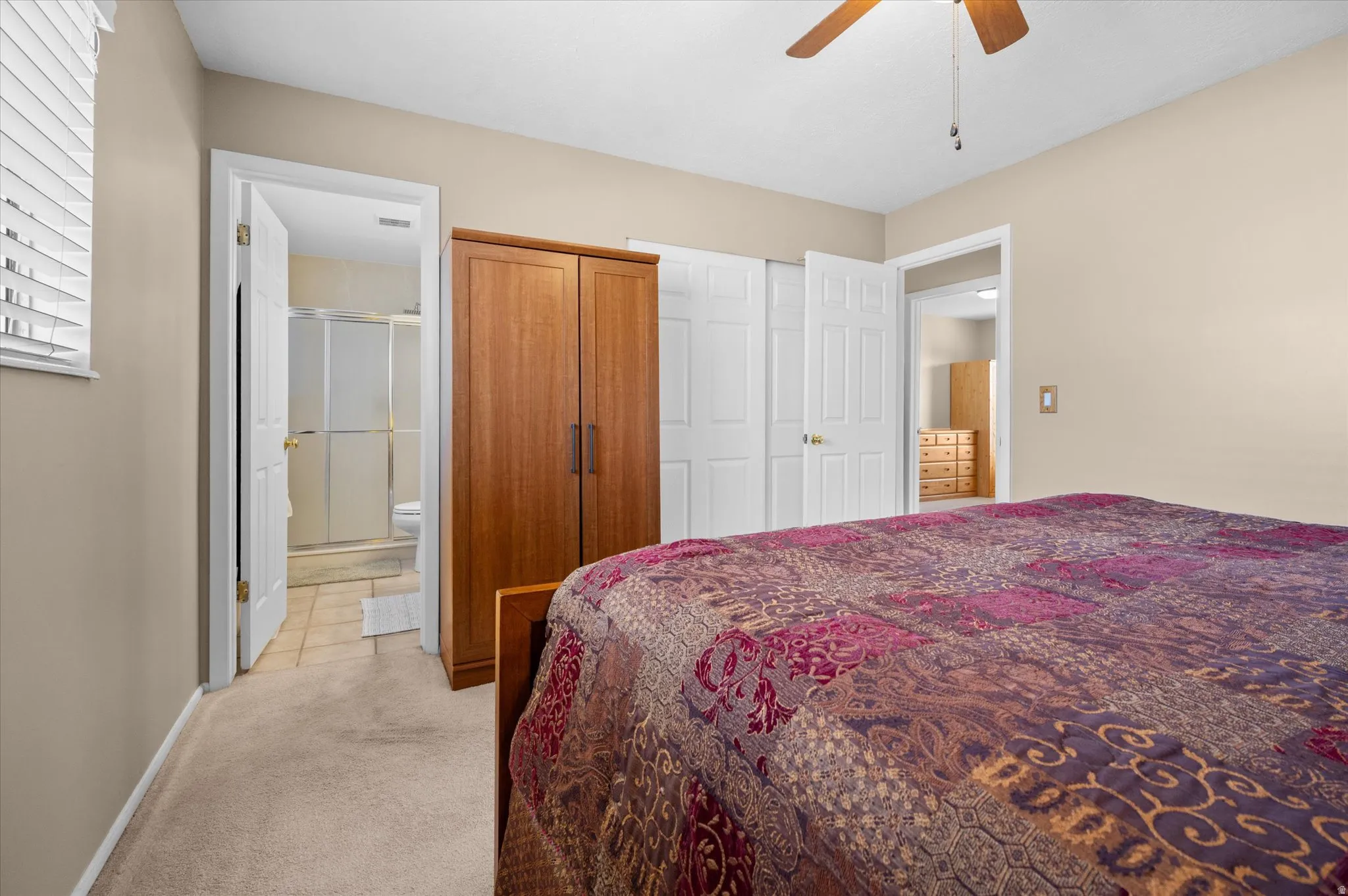 Bedroom featuring light colored carpet, ceiling fan, connected bathroom, and a closet