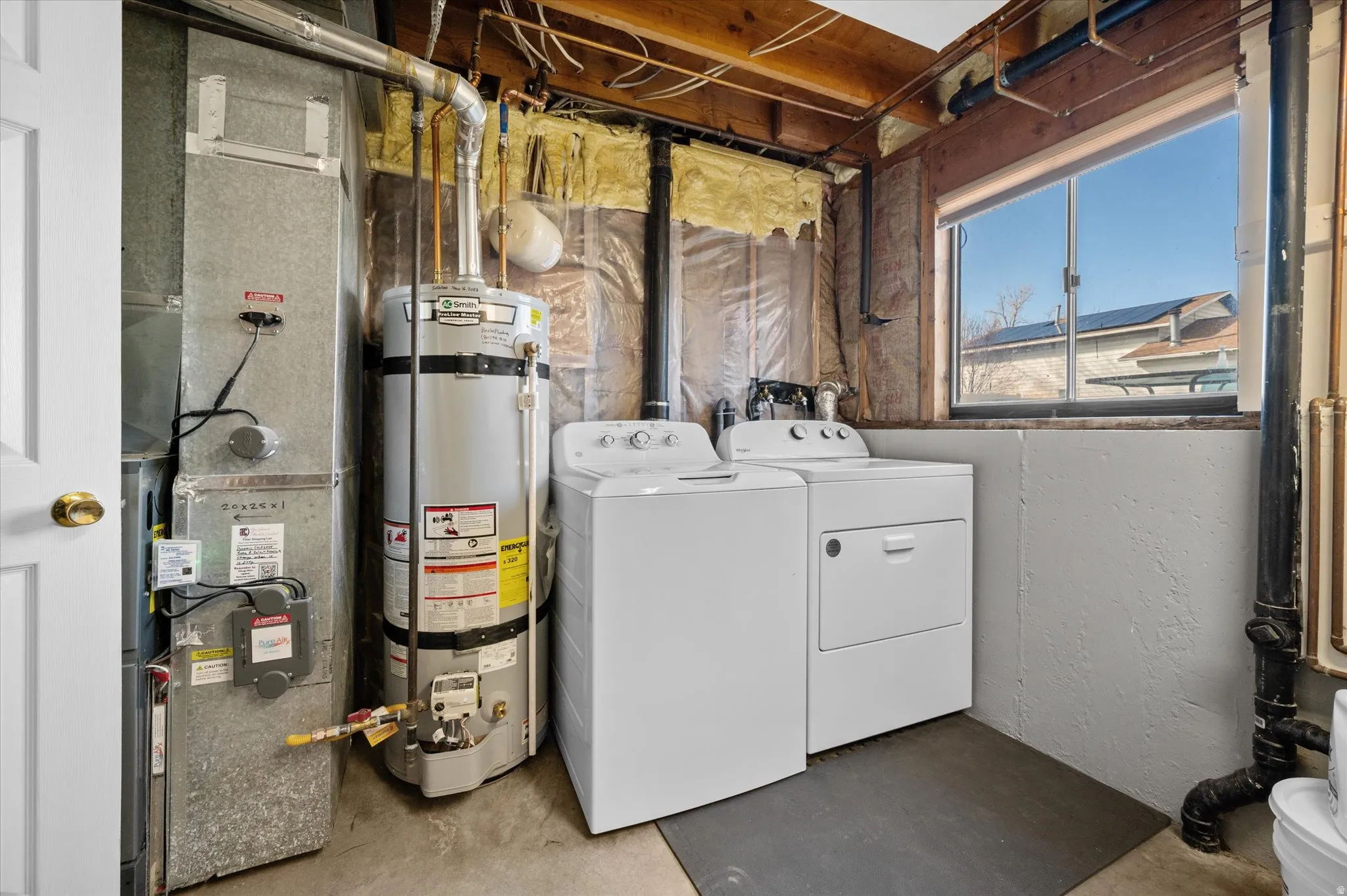 Laundry area featuring concrete floors, water heater, heating unit, and washing machine and clothes dryer