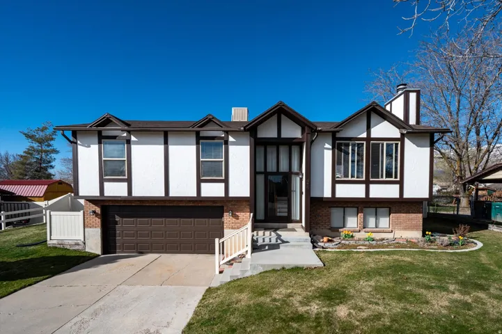 View of front of home with a chimney, an attached garage, driveway, and brick siding
