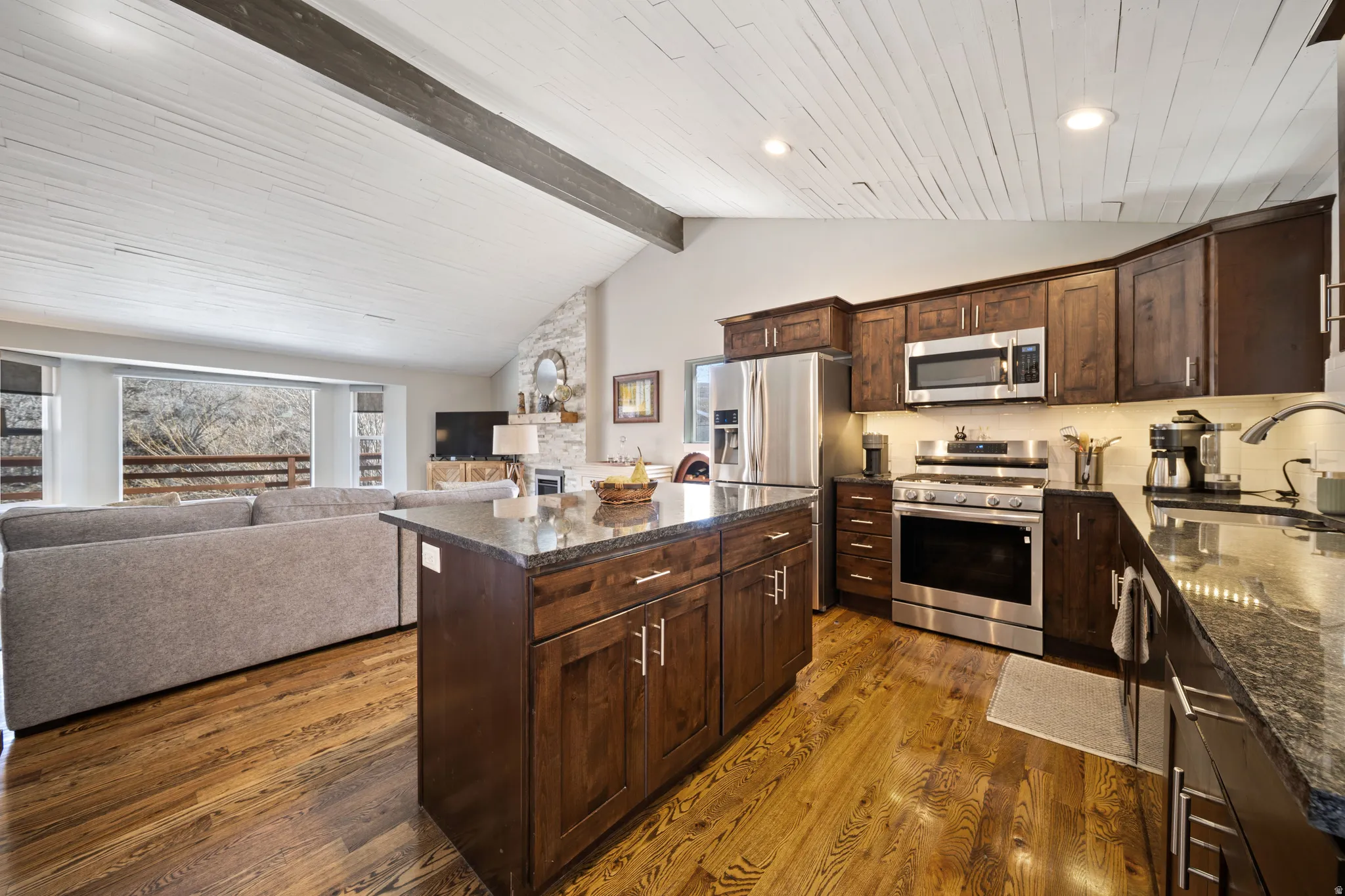 Kitchen featuring dark wood finish cabinetry, vaulted ceiling, stainless steel appliances, open floor plan, and a kitchen island