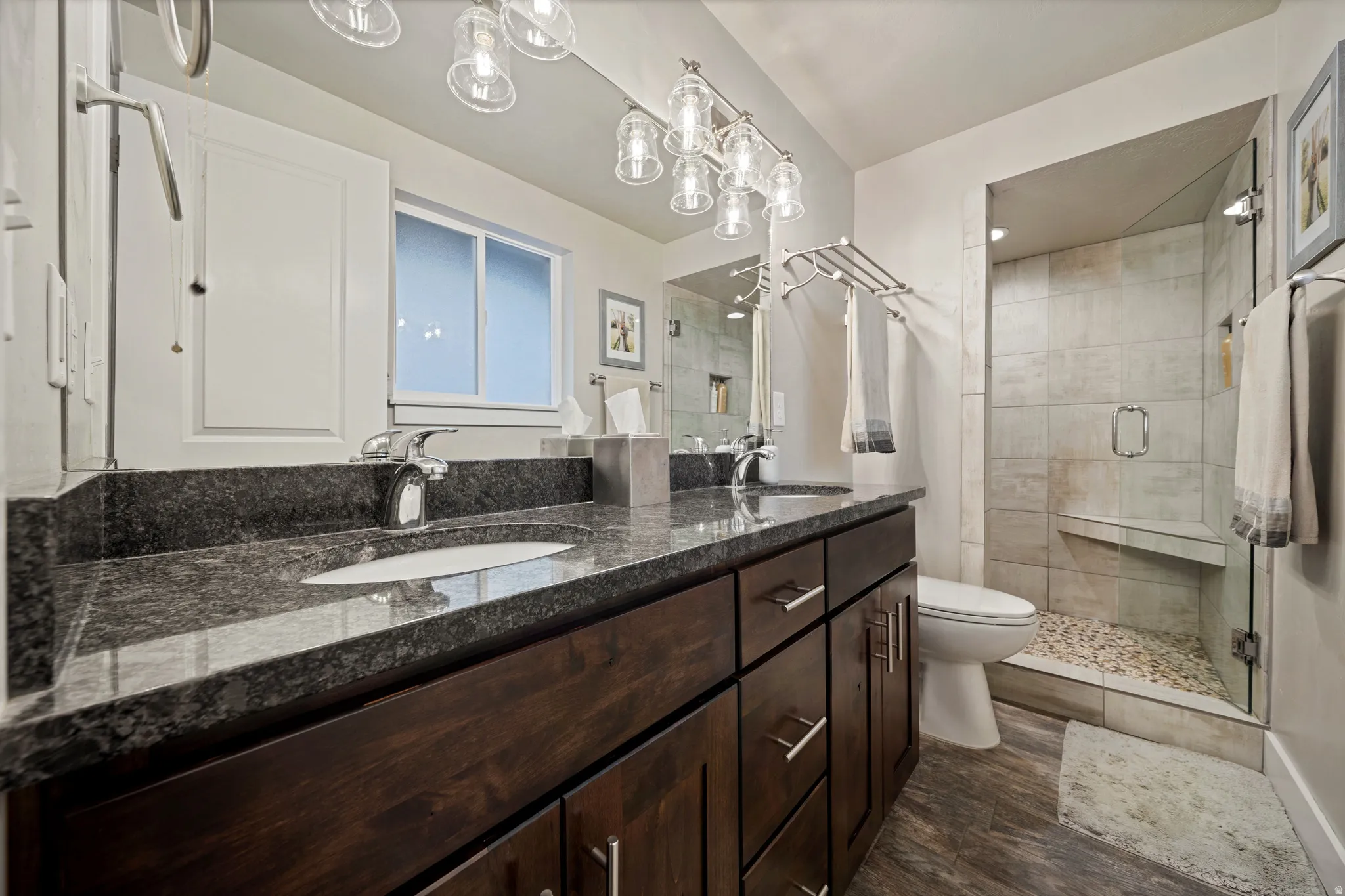Full bath featuring double vanity, a stall shower, and dark wood-type flooring