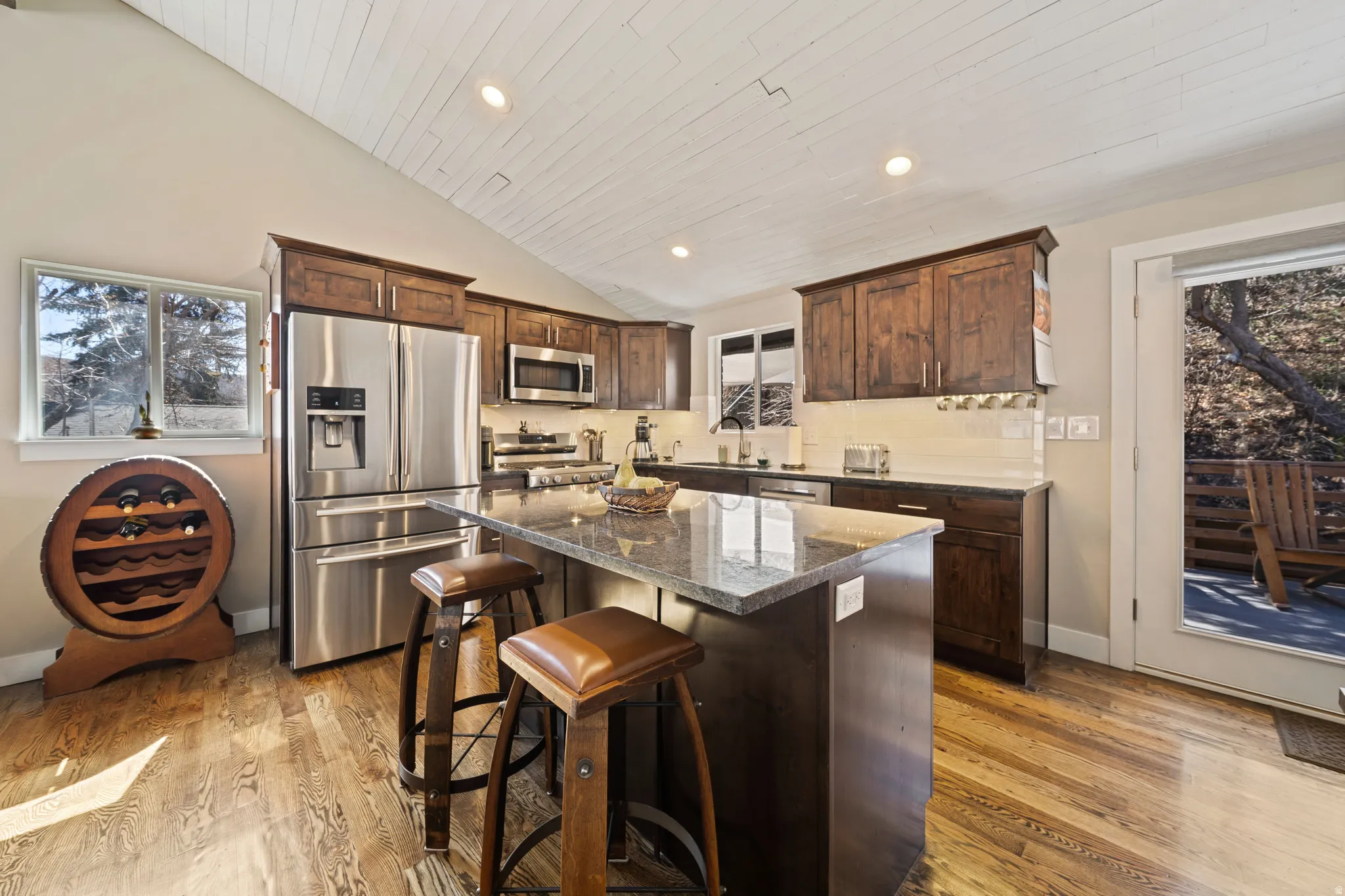 Kitchen featuring dark wood finish cabinets, stainless steel appliances, a breakfast bar, light wood-style floors, and dark stone countertops