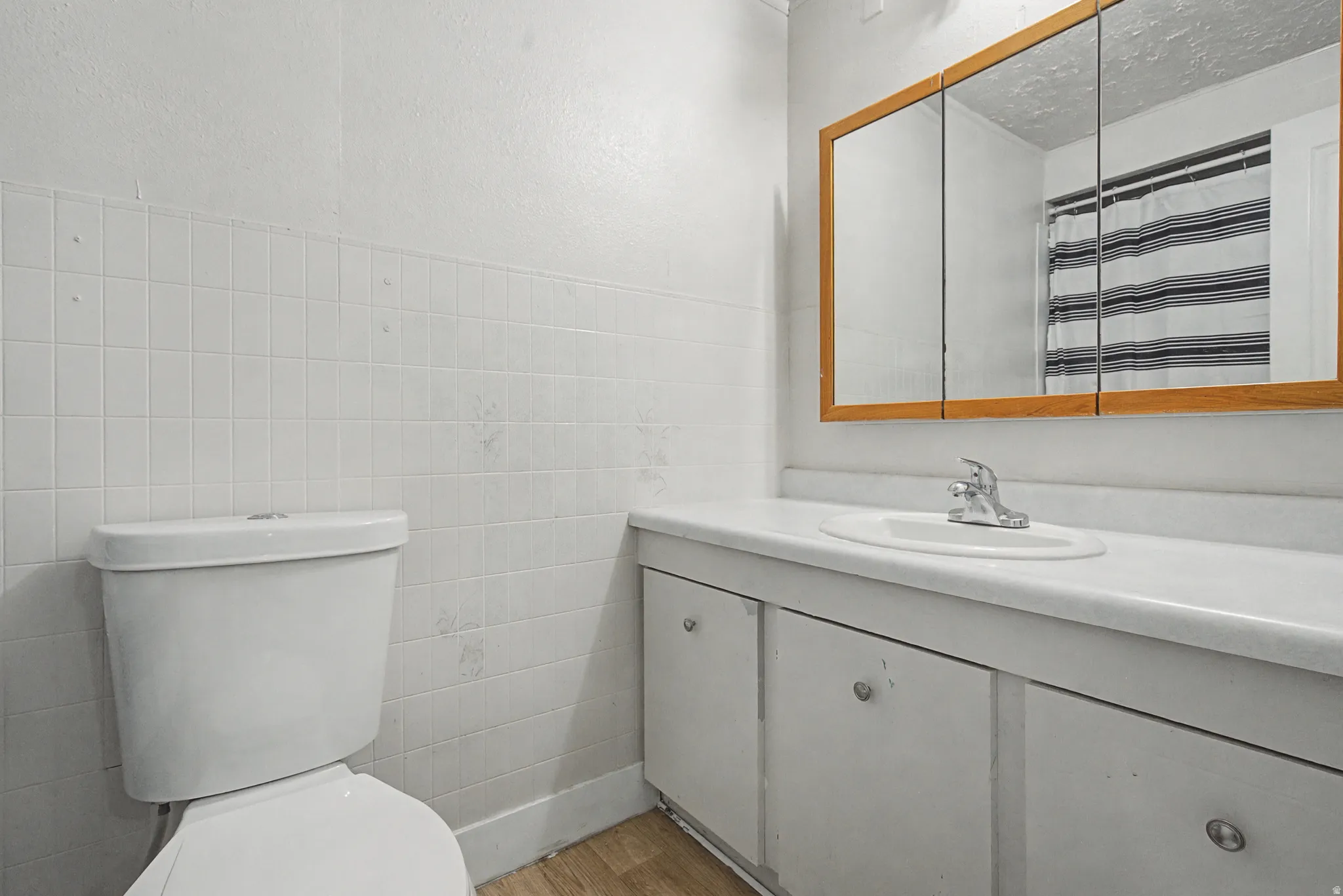 Bathroom with vanity, light wood-style floors, curtained shower, tile walls, and a textured ceiling