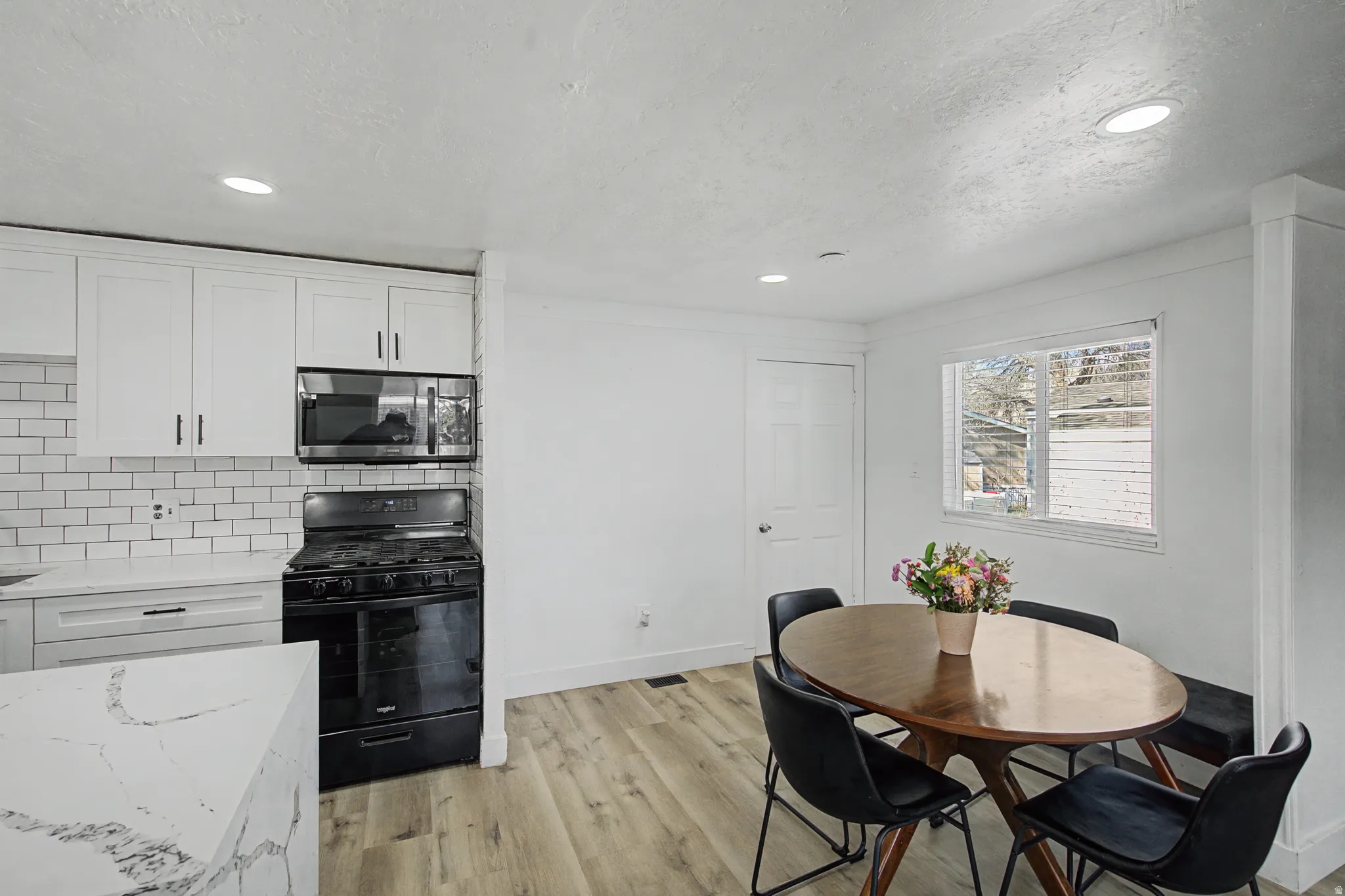 Kitchen featuring black range with gas cooktop, white cabinets, stainless steel microwave, light wood-style flooring, and decorative backsplash