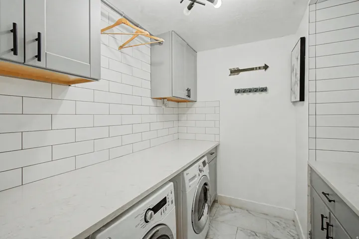 Laundry room with washing machine and clothes dryer, cabinet space, and light marble finish floors