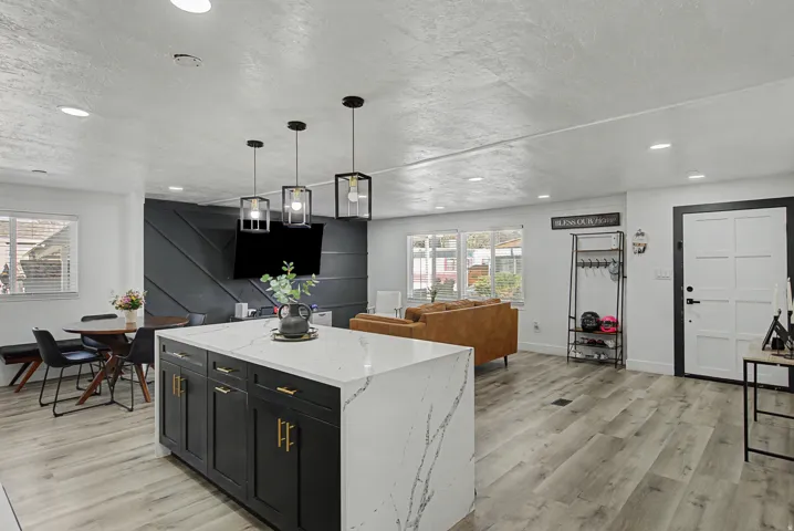 Kitchen with dark cabinetry, a center island, decorative light fixtures, light stone counters, and light wood-type flooring