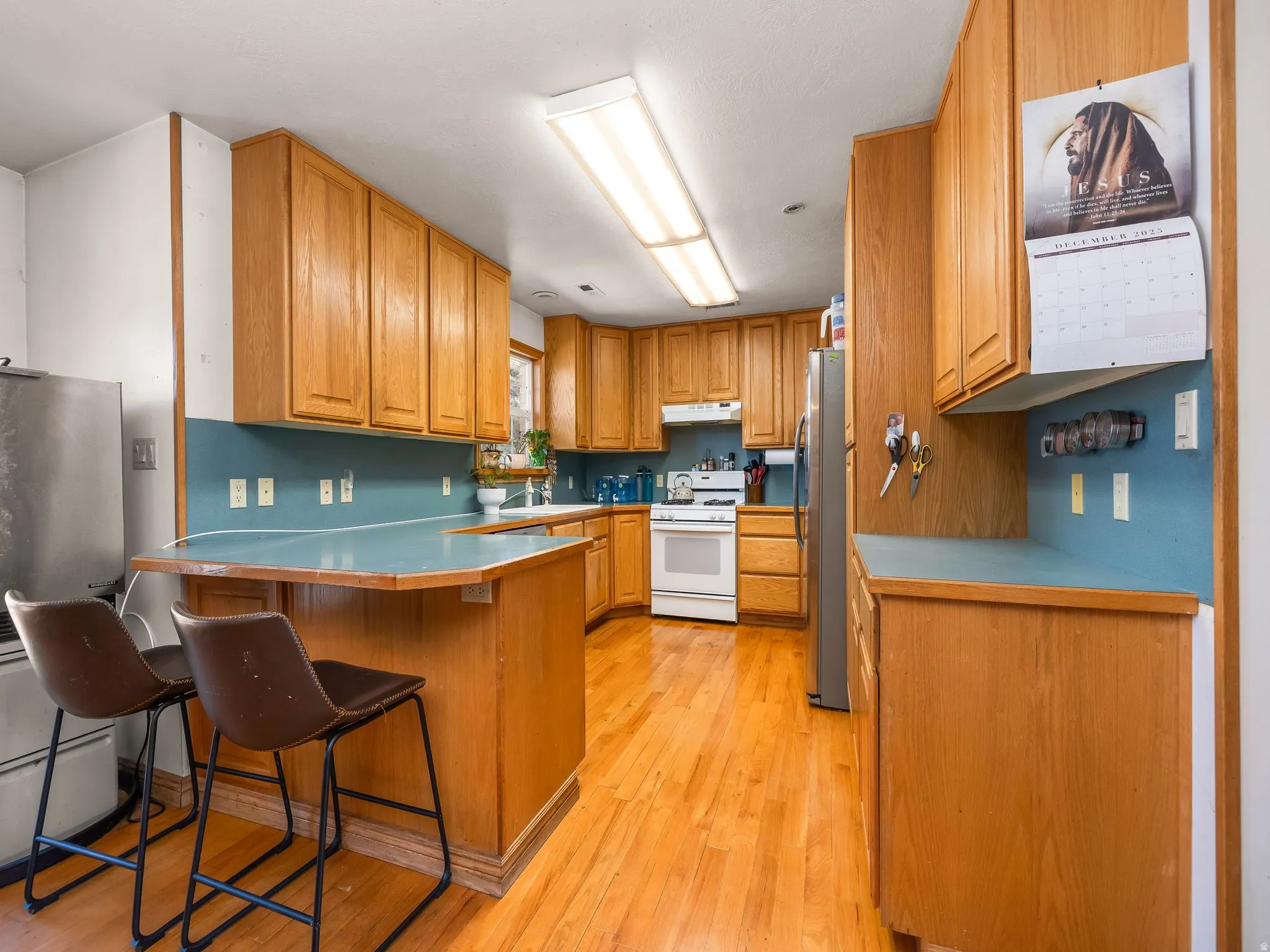 Kitchen featuring wood finish cabinets, a peninsula, a breakfast bar, white gas range oven, and light wood finished floors