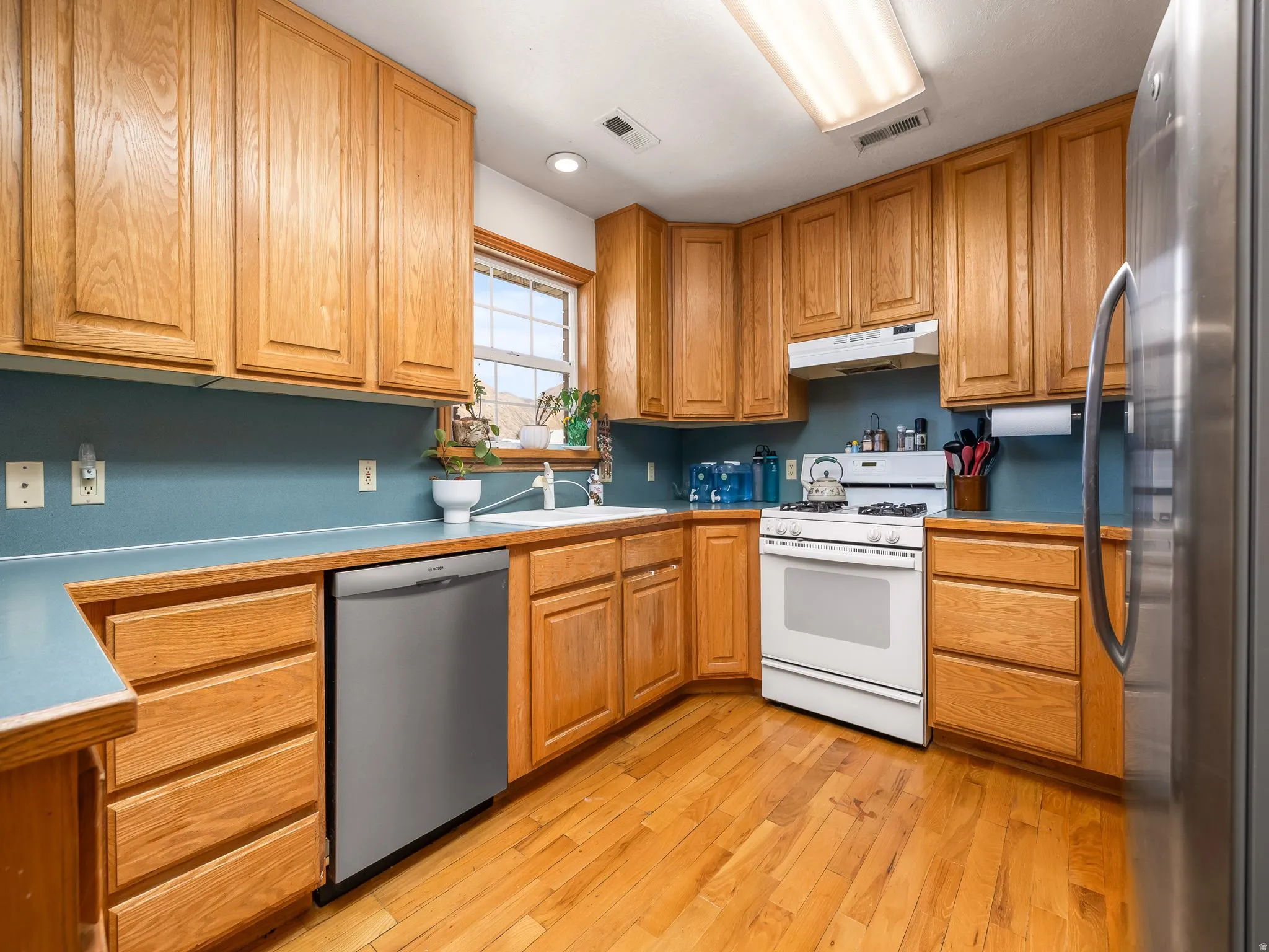 Kitchen featuring stainless steel appliances, light wood-type flooring, wood finish cabinets, and light countertops