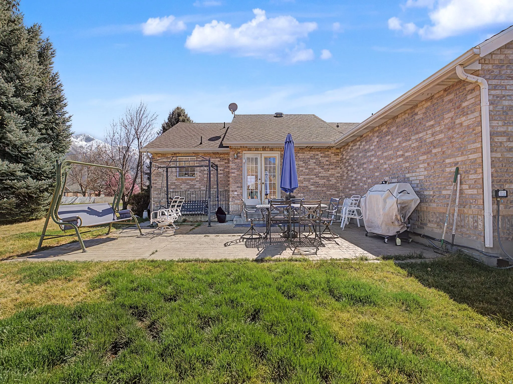 Back of property featuring a patio, a lawn, roof with shingles, brick siding, and outdoor dining area