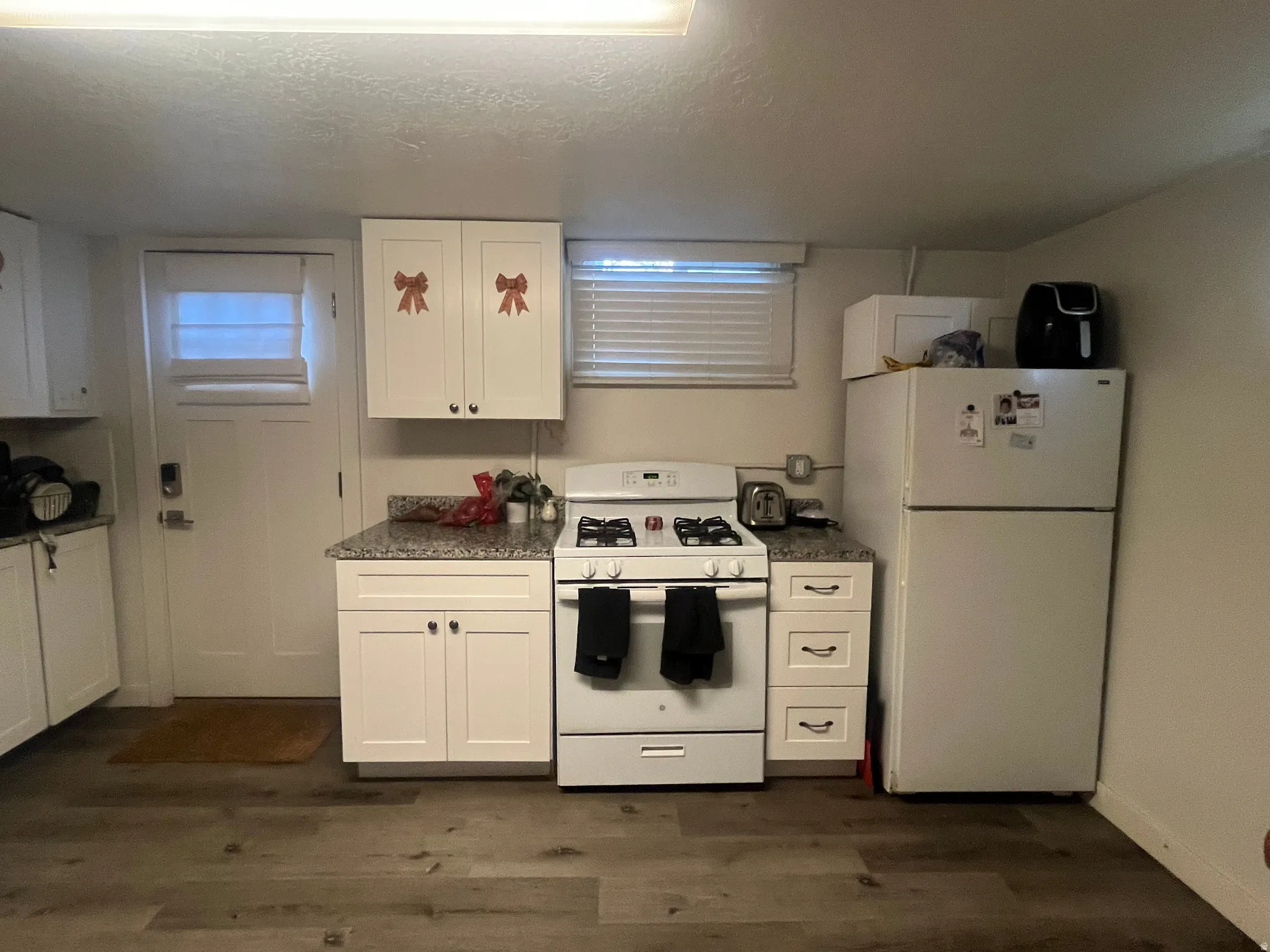 Kitchen with white appliances, white cabinetry, a textured ceiling, dark wood-type flooring, and dark countertops