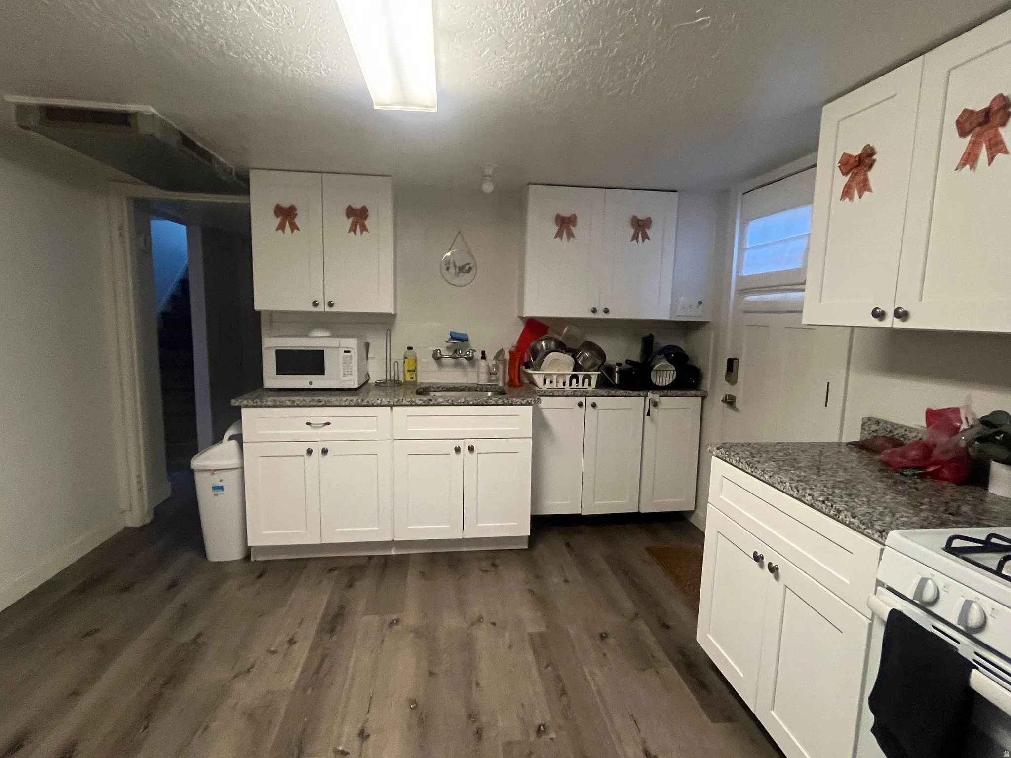 Kitchen with white appliances, white cabinets, dark wood-style flooring, a textured ceiling, and dark stone counters