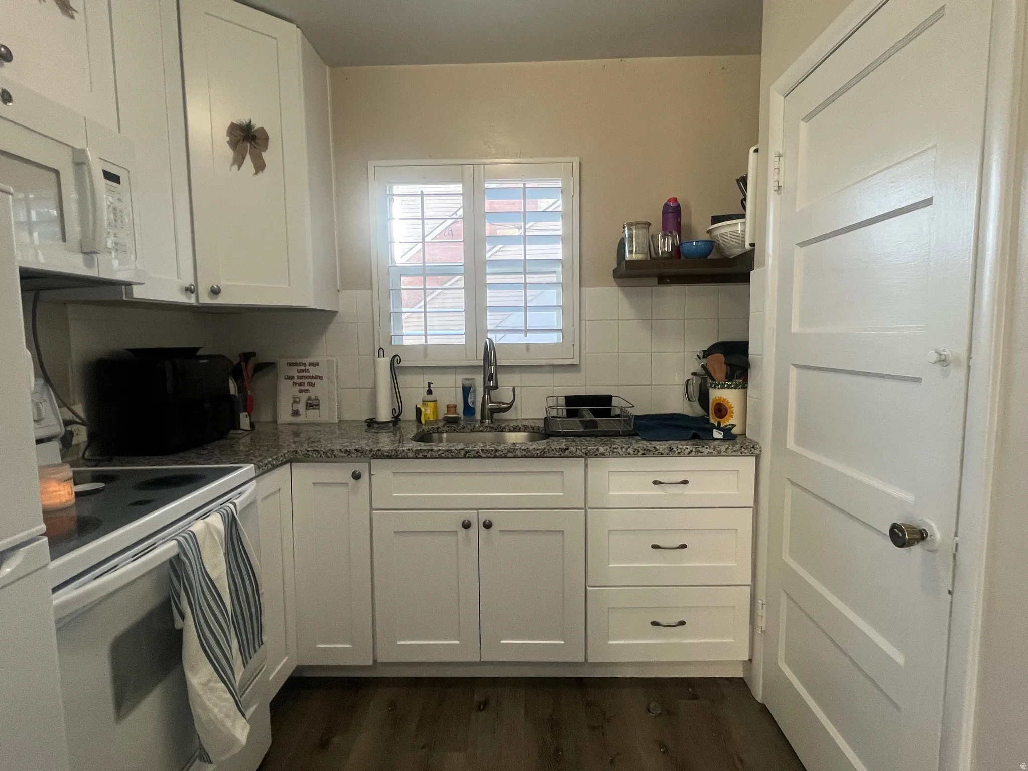 Kitchen with white cabinets, white appliances, dark wood-style floors, and dark stone counters