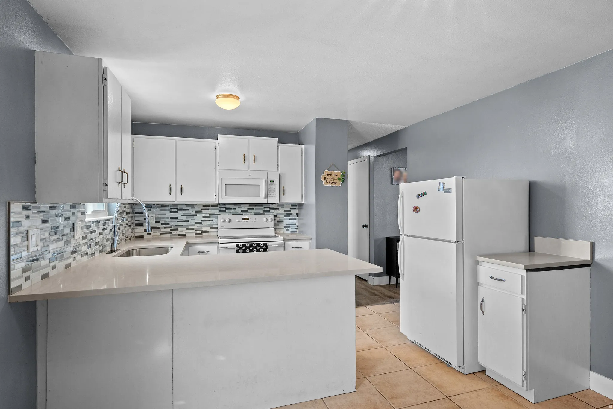 Kitchen featuring white cabinetry, white appliances, decorative backsplash, a peninsula, and light tile patterned flooring