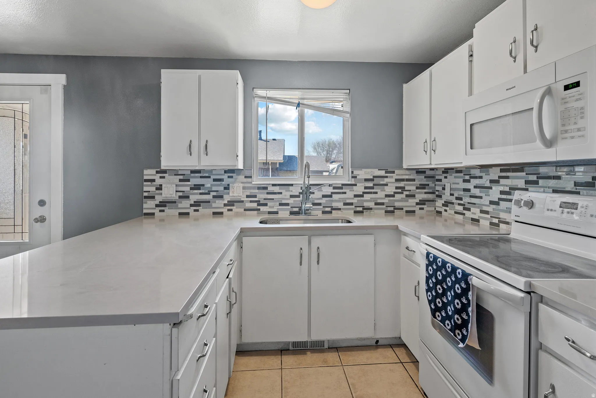 Kitchen featuring white appliances, a peninsula, light countertops, white cabinets, and light tile patterned flooring