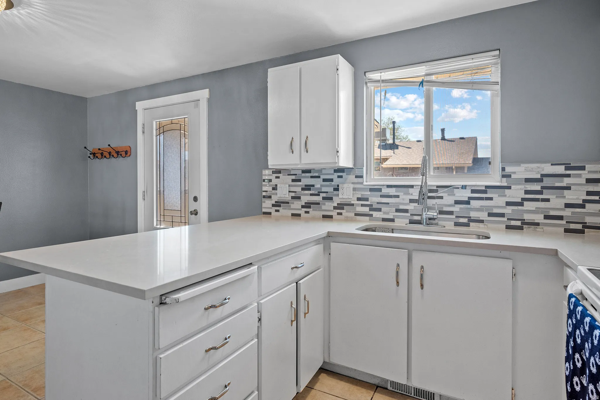 Kitchen with white cabinetry, a peninsula, light tile patterned floors, stove, and tasteful backsplash