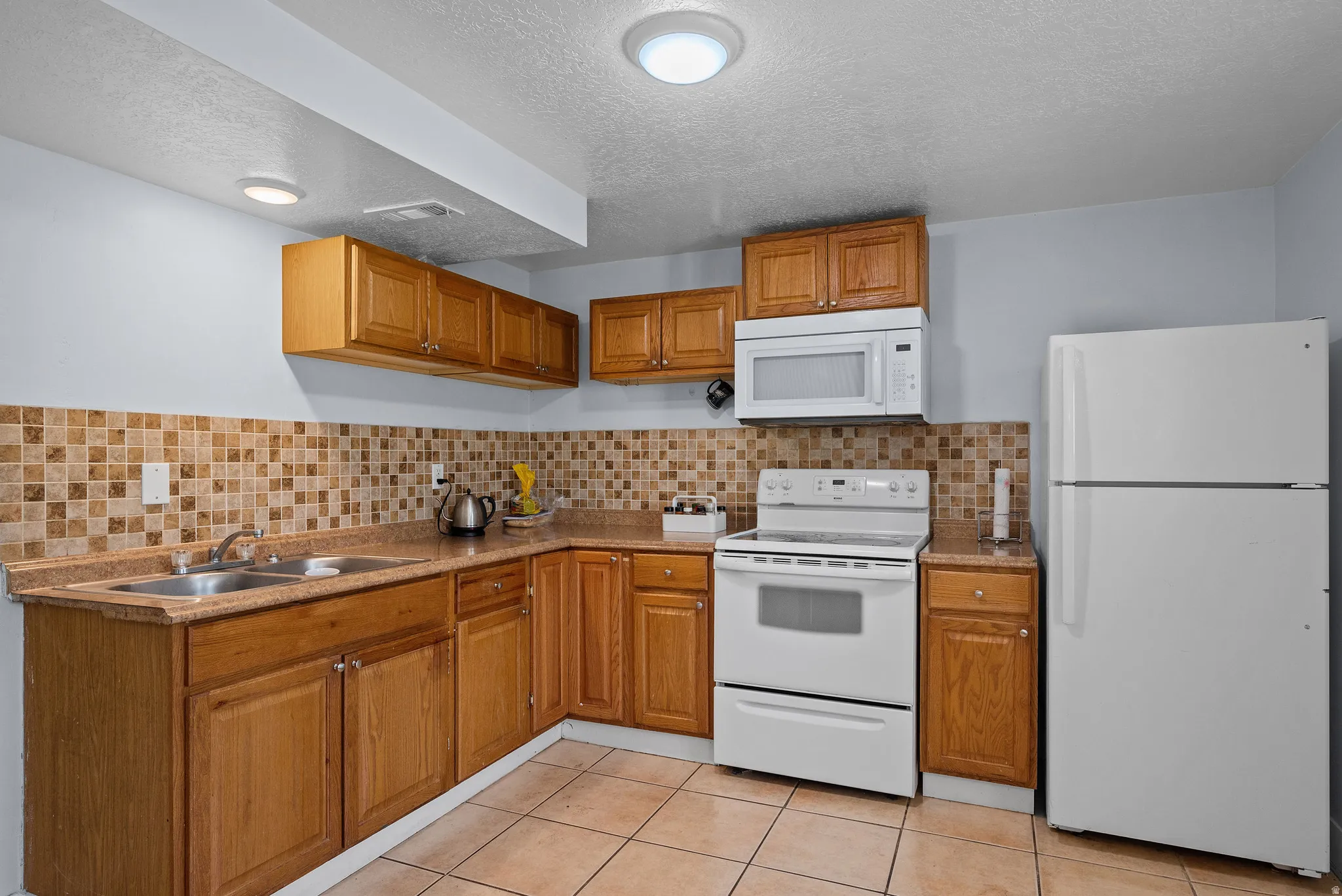 Kitchen featuring white appliances, wood finish cabinets, light tile patterned floors, light countertops, and a textured ceiling