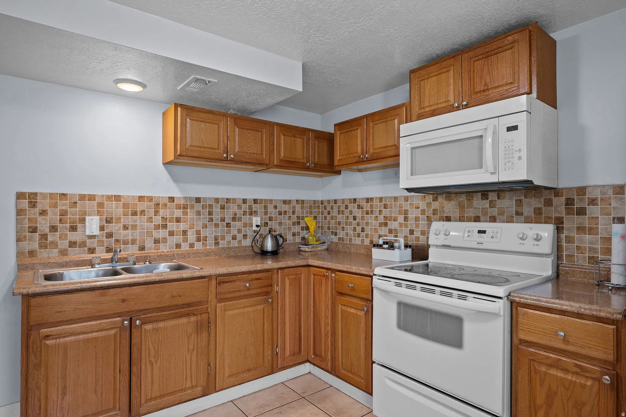 Kitchen with white appliances, wood finish cabinetry, light tile patterned floors, a textured ceiling, and light countertops