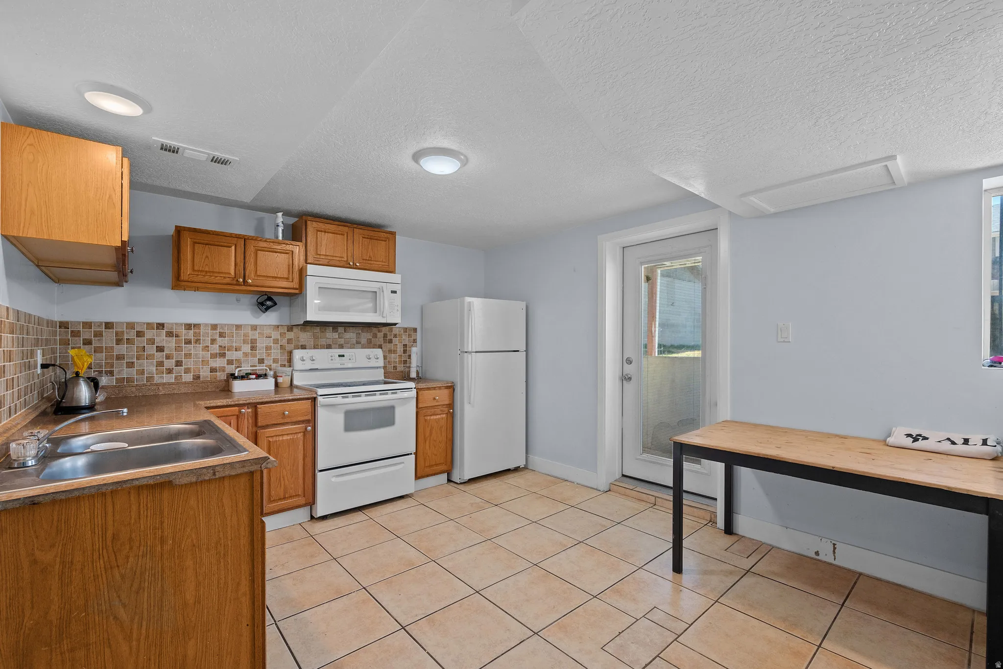 Kitchen featuring white appliances, a textured ceiling, backsplash, wood finish cabinetry, and light tile patterned floors