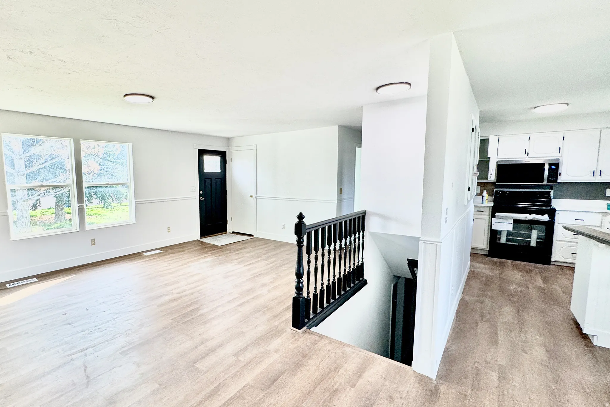 Kitchen with white cabinetry, black range with electric cooktop, light wood-style flooring, stainless steel microwave, and light countertops