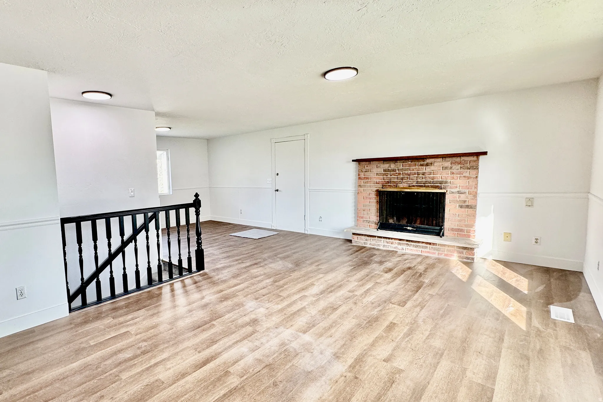 Unfurnished living room with light wood-type flooring, a textured ceiling, and a fireplace