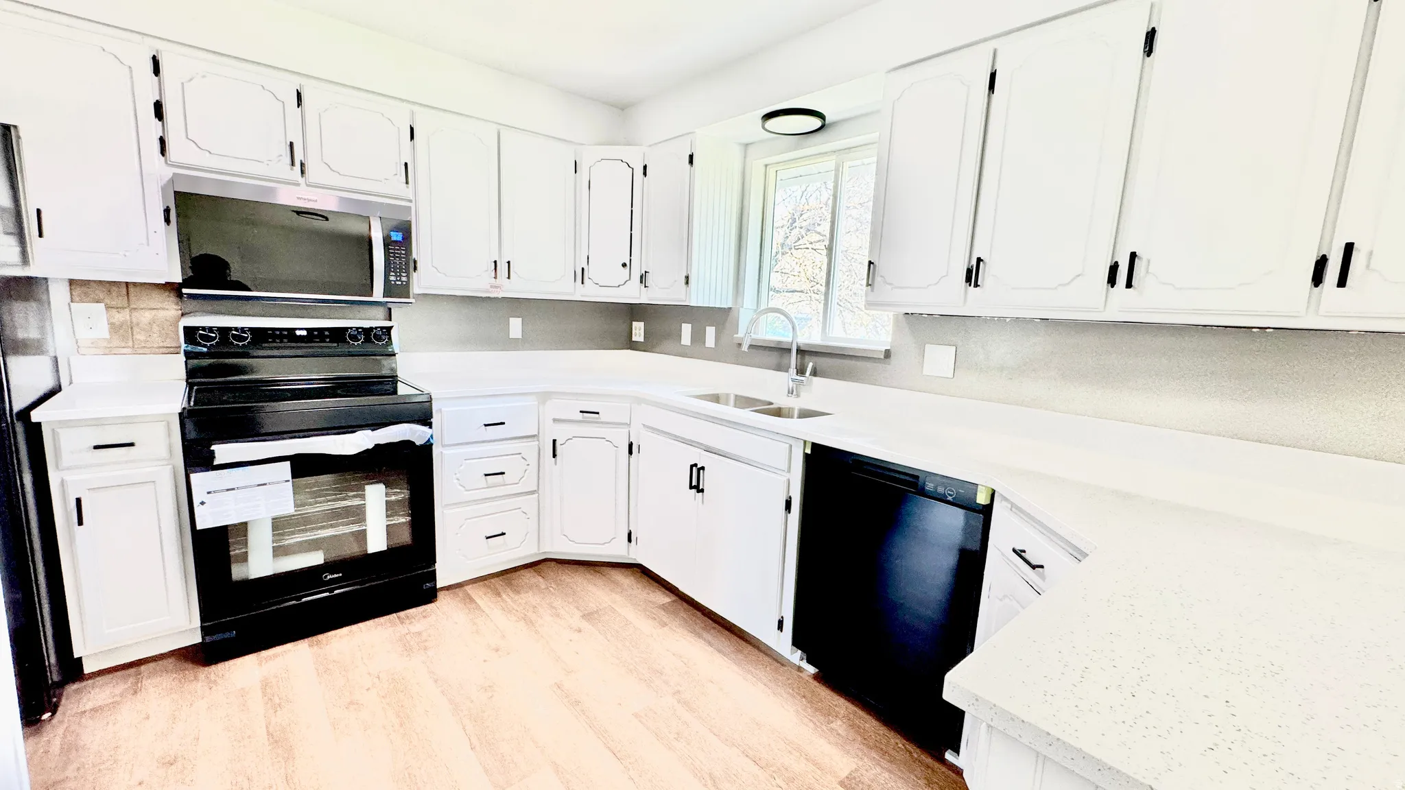 Kitchen with black appliances, white cabinetry, light wood-style floors, and light stone counters