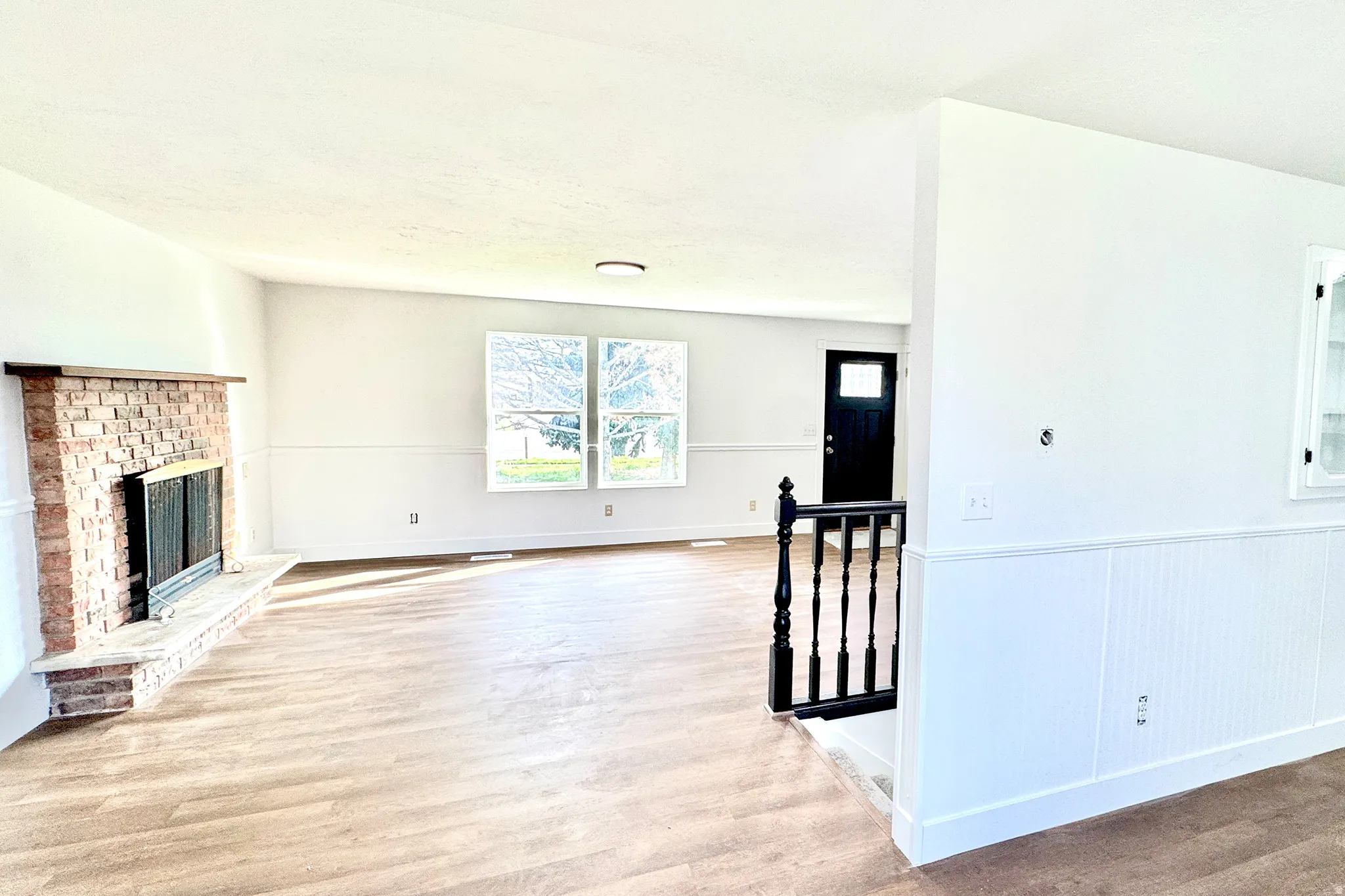 Unfurnished living room featuring light wood-style flooring, a fireplace, and wainscoting