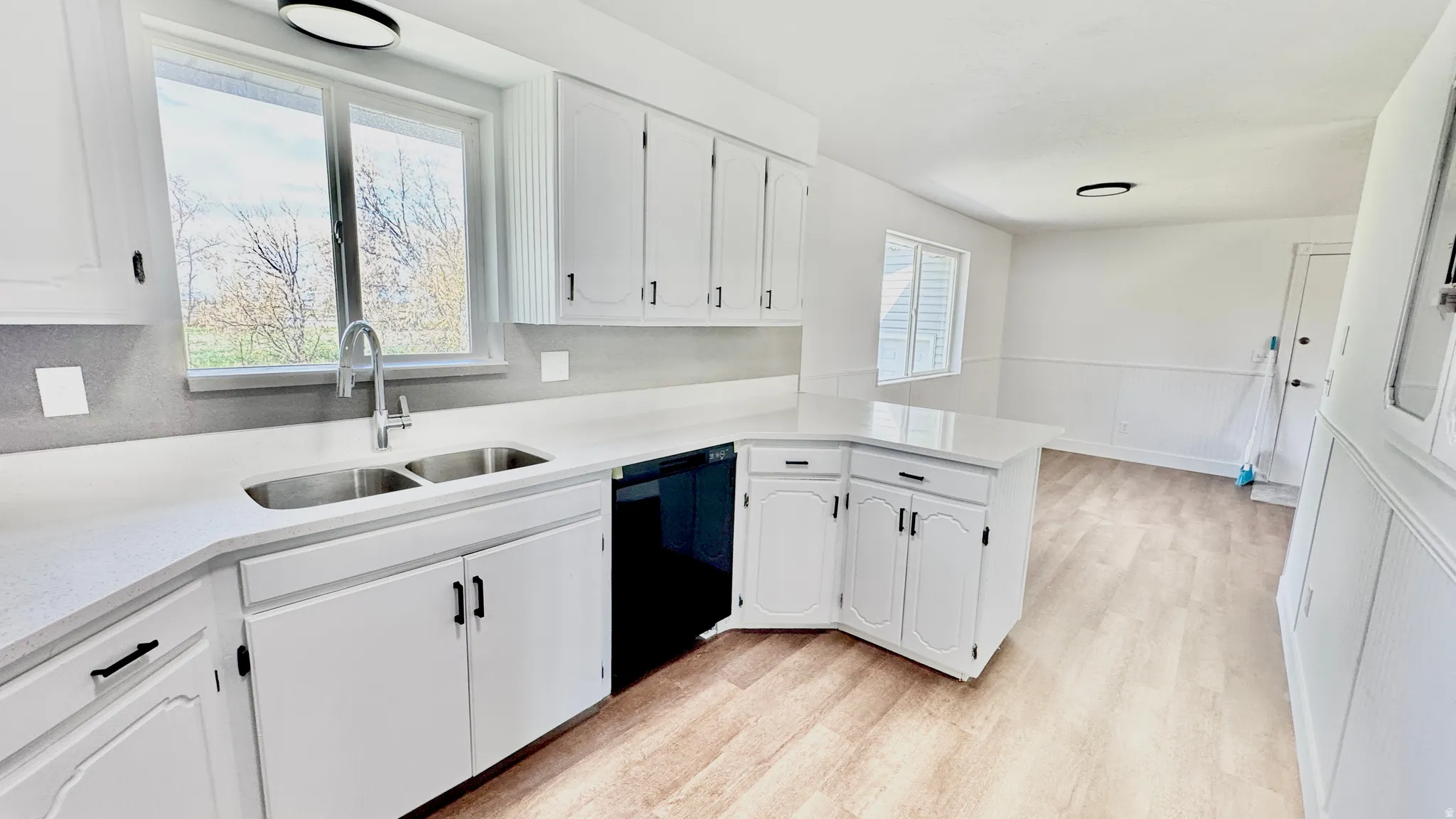 Kitchen featuring a wainscoted wall, light stone countertops, light wood-type flooring, white cabinets, and black dishwasher