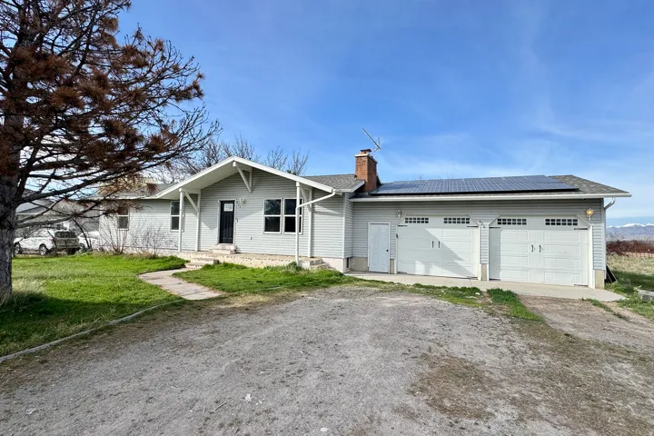 View of front of property with roof mounted solar panels, dirt driveway, a chimney, an attached garage, and a front yard