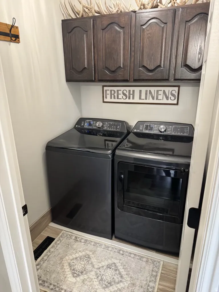Laundry room with light wood-style flooring, separate washer and dryer, and cabinet space