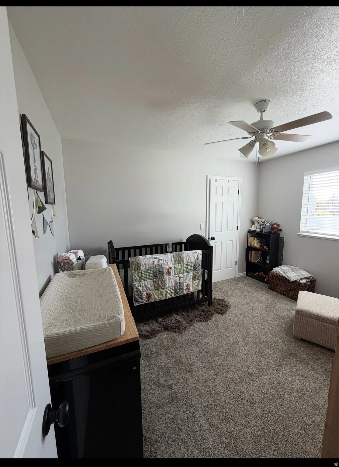 Bedroom featuring carpet flooring, a nursery area, a textured ceiling, and a ceiling fan