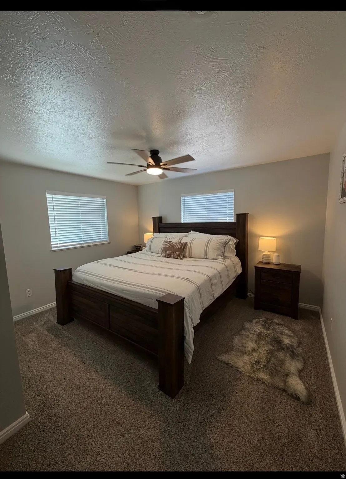 Carpeted bedroom with ceiling fan, a textured ceiling, and multiple windows