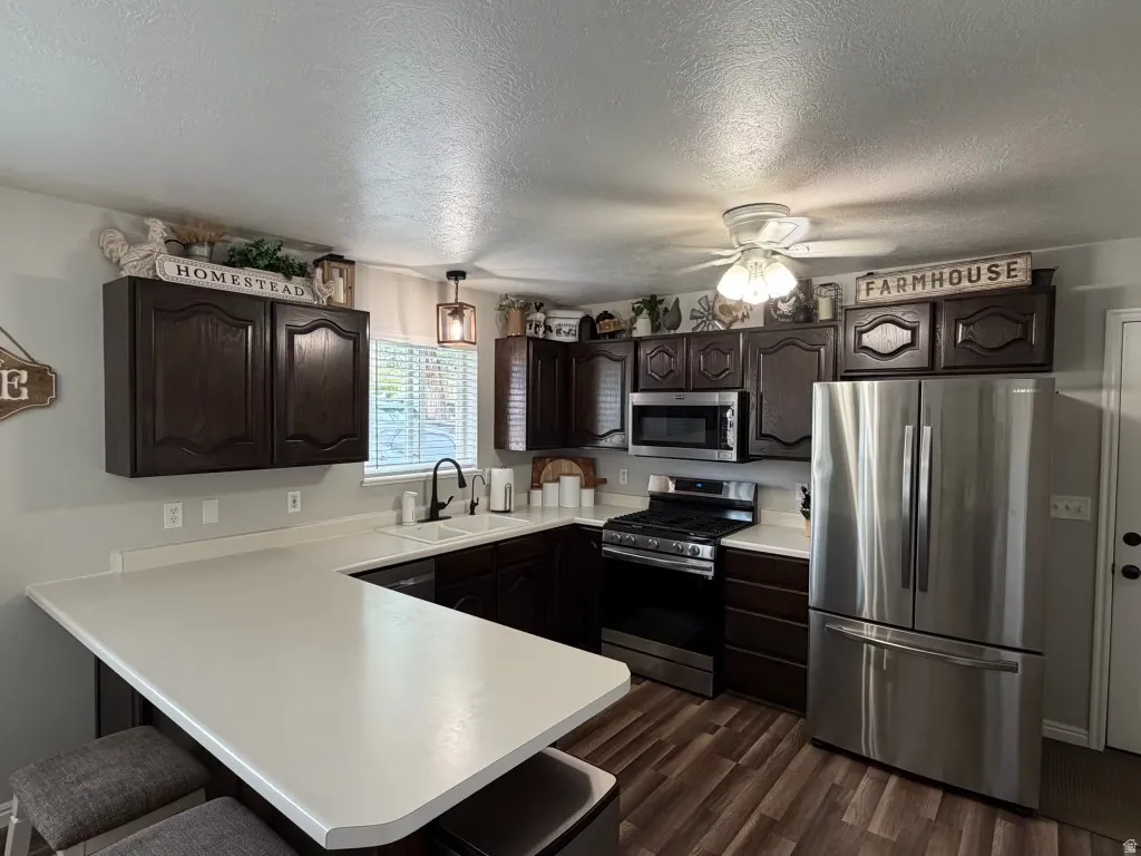 Kitchen featuring dark wood finish cabinets, stainless steel appliances, a kitchen bar, a peninsula, and a textured ceiling