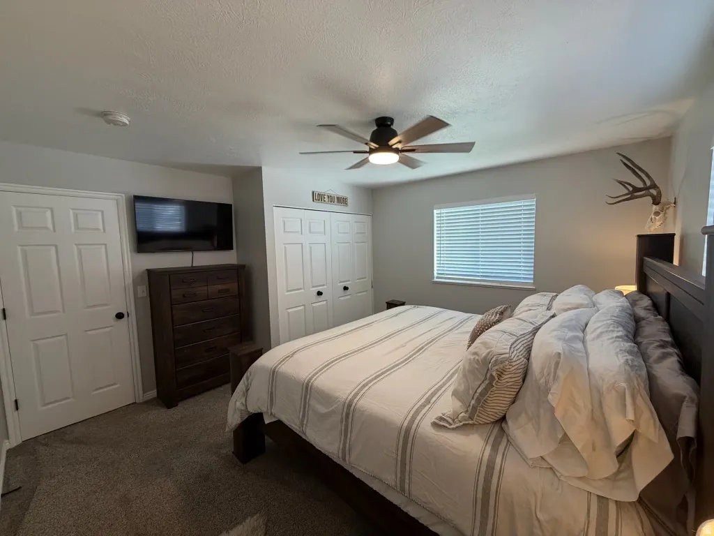 Bedroom with dark colored carpet, a closet, ceiling fan, and a textured ceiling