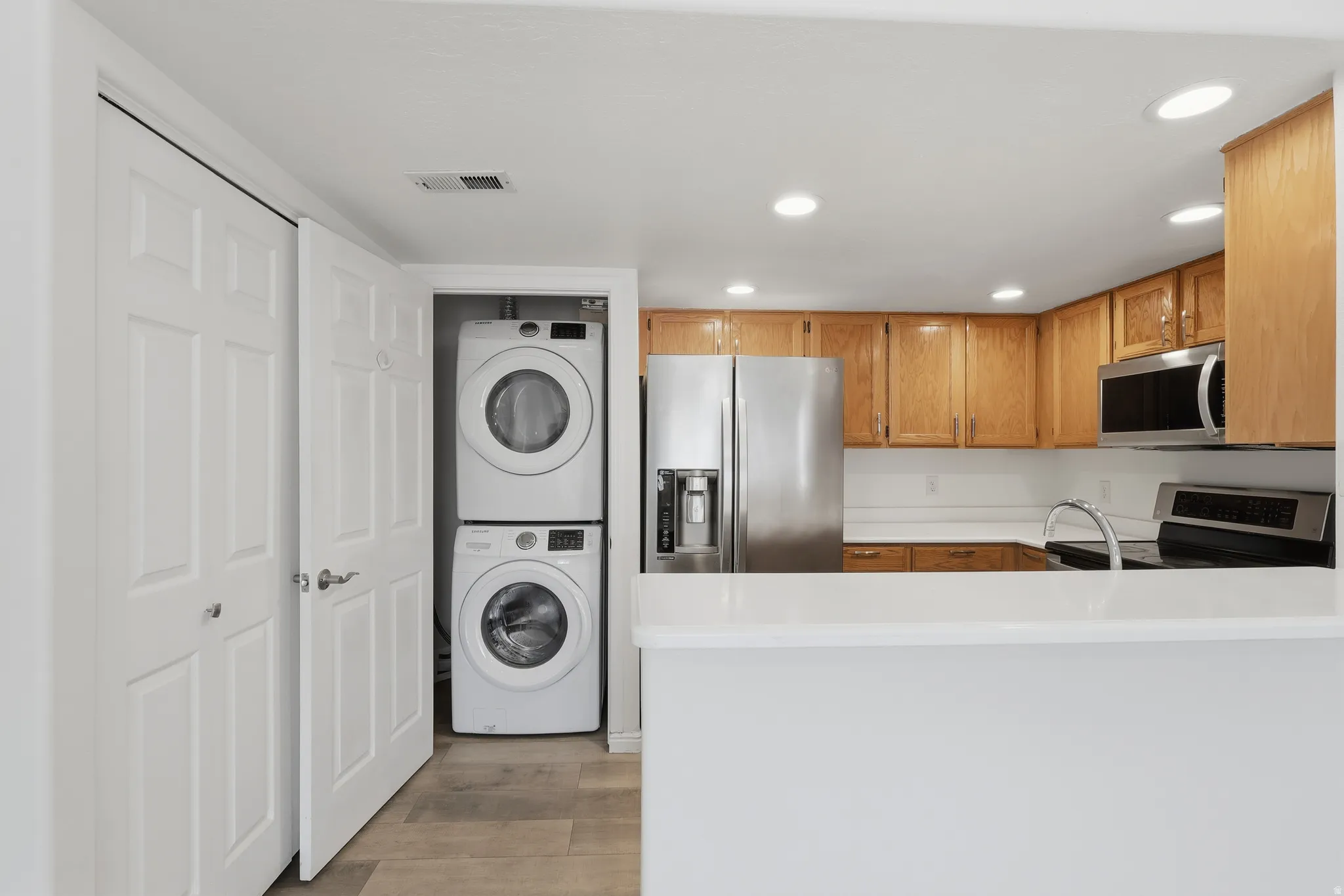 Kitchen with stainless steel appliances, light countertops, recessed lighting, light wood finished floors, and stacked washer / dryer