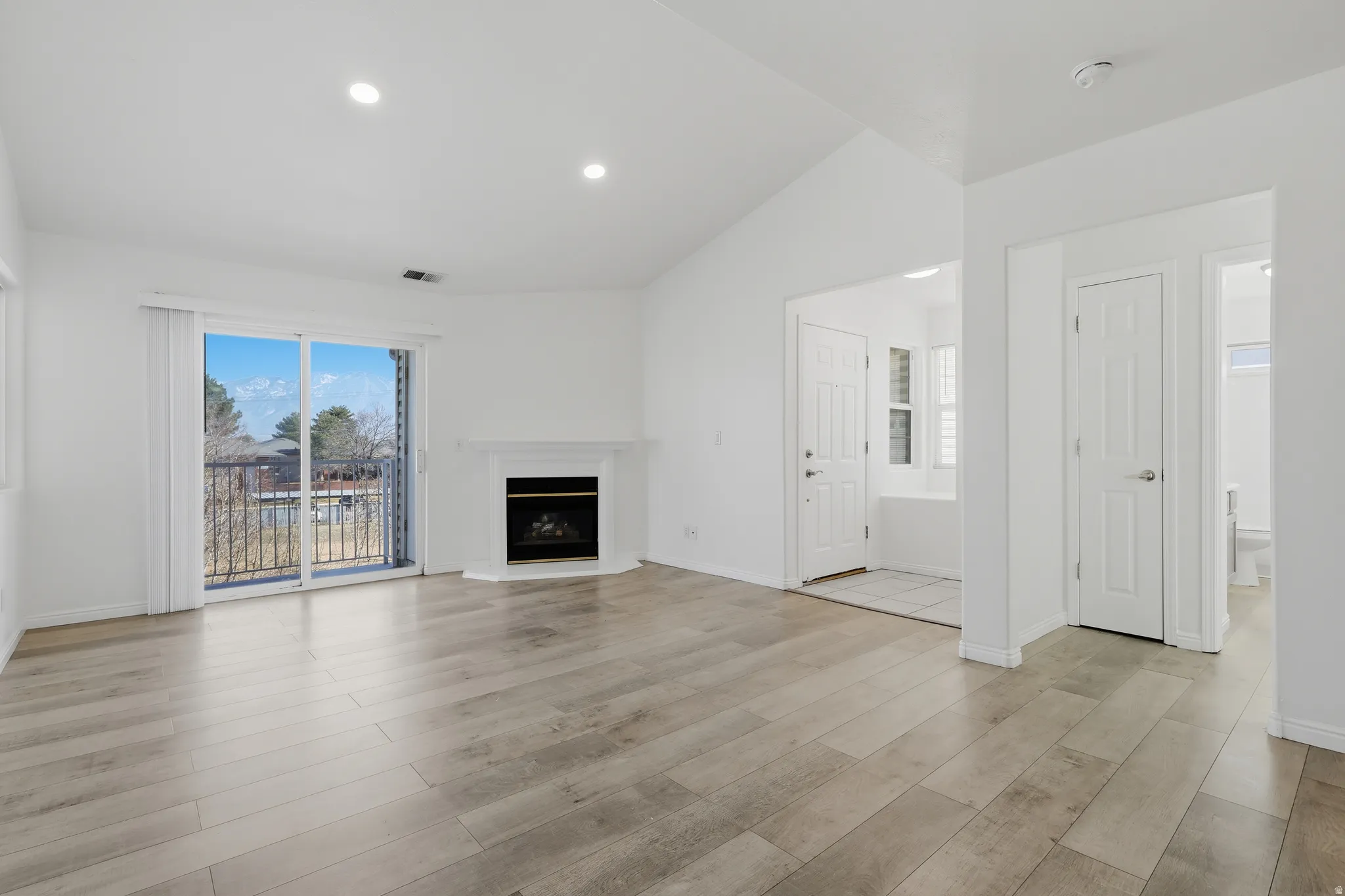 Unfurnished living room with vaulted ceiling, light wood-style floors, a fireplace with raised hearth, plenty of natural light, and recessed lighting