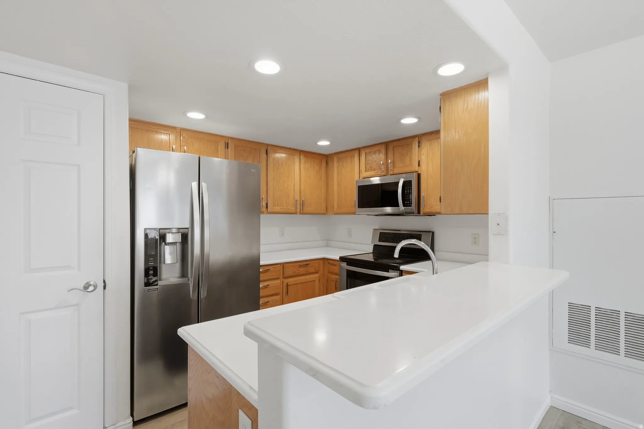 Kitchen featuring recessed lighting, stainless steel appliances, a peninsula, light countertops, and light wood-style flooring