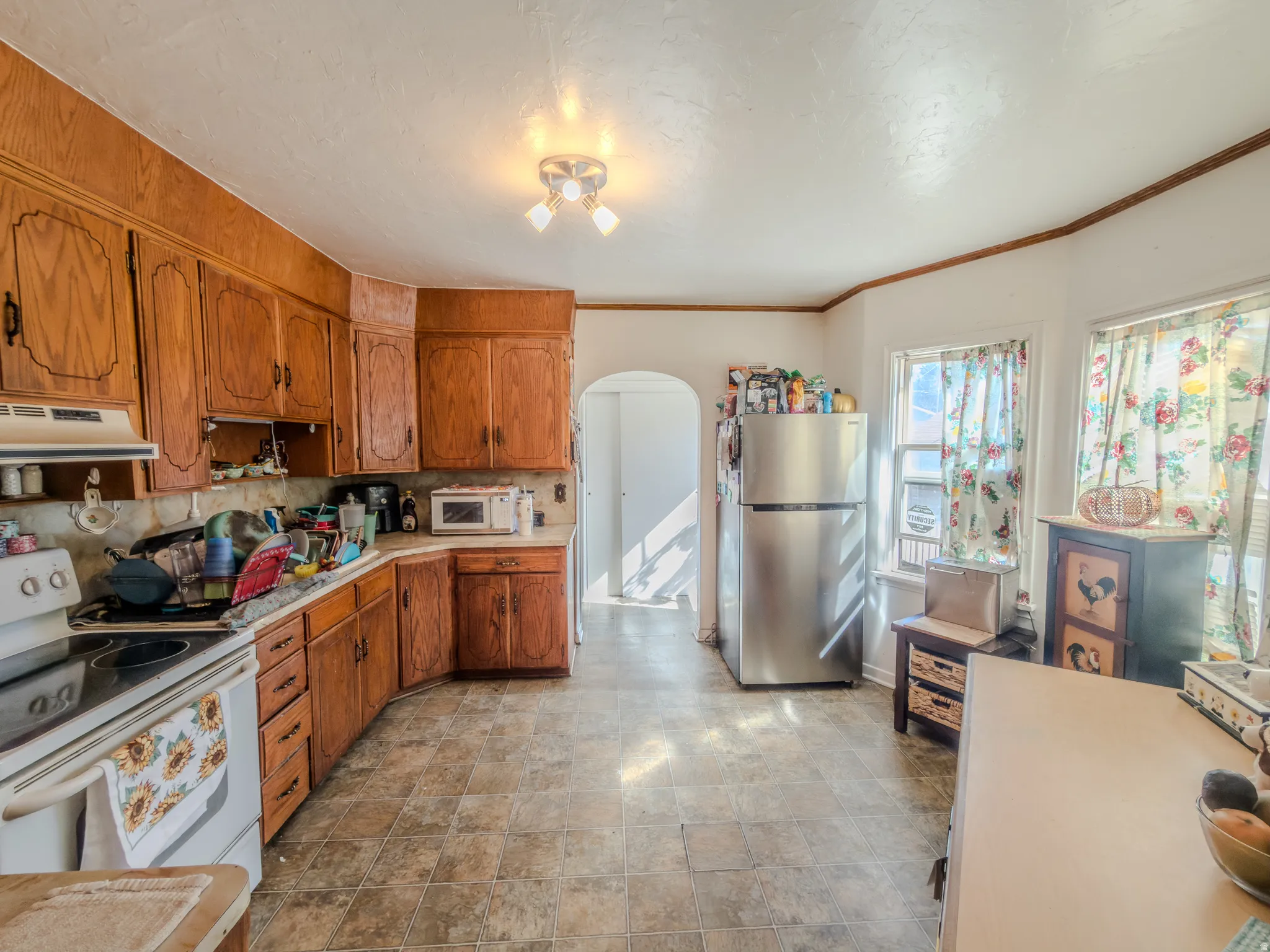 Kitchen with arched walkways, wood finish cabinets, white appliances, light countertops, and stone finish flooring
