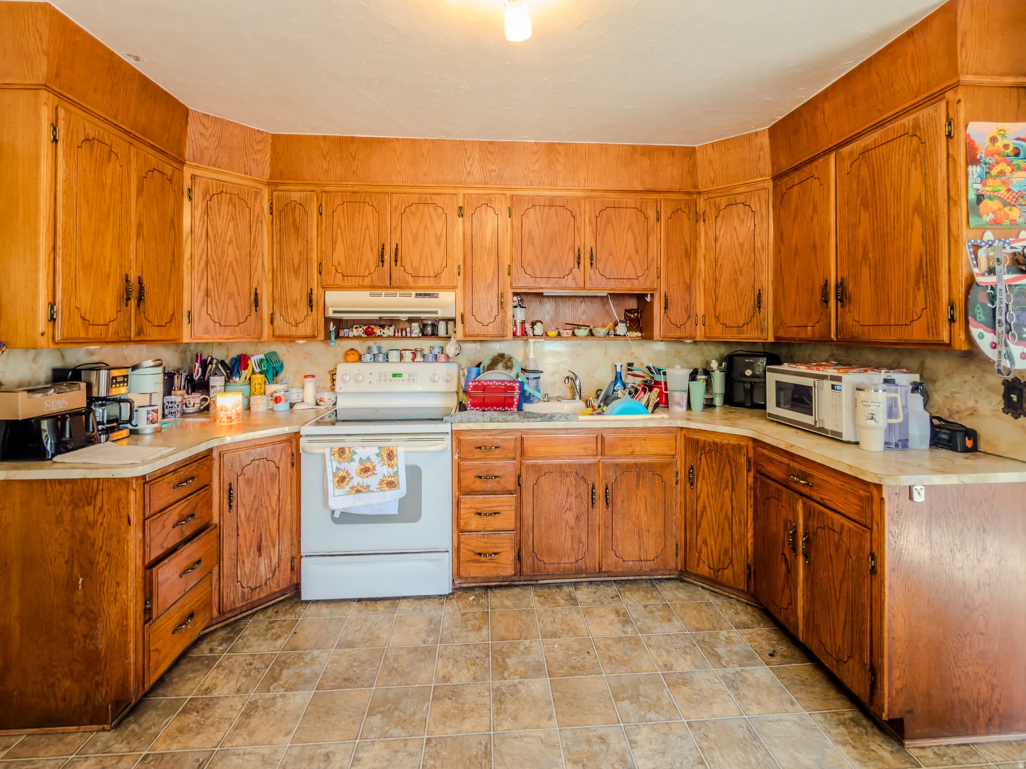 Kitchen with white range with electric cooktop, wood finish cabinets, light countertops, and stone finish flooring