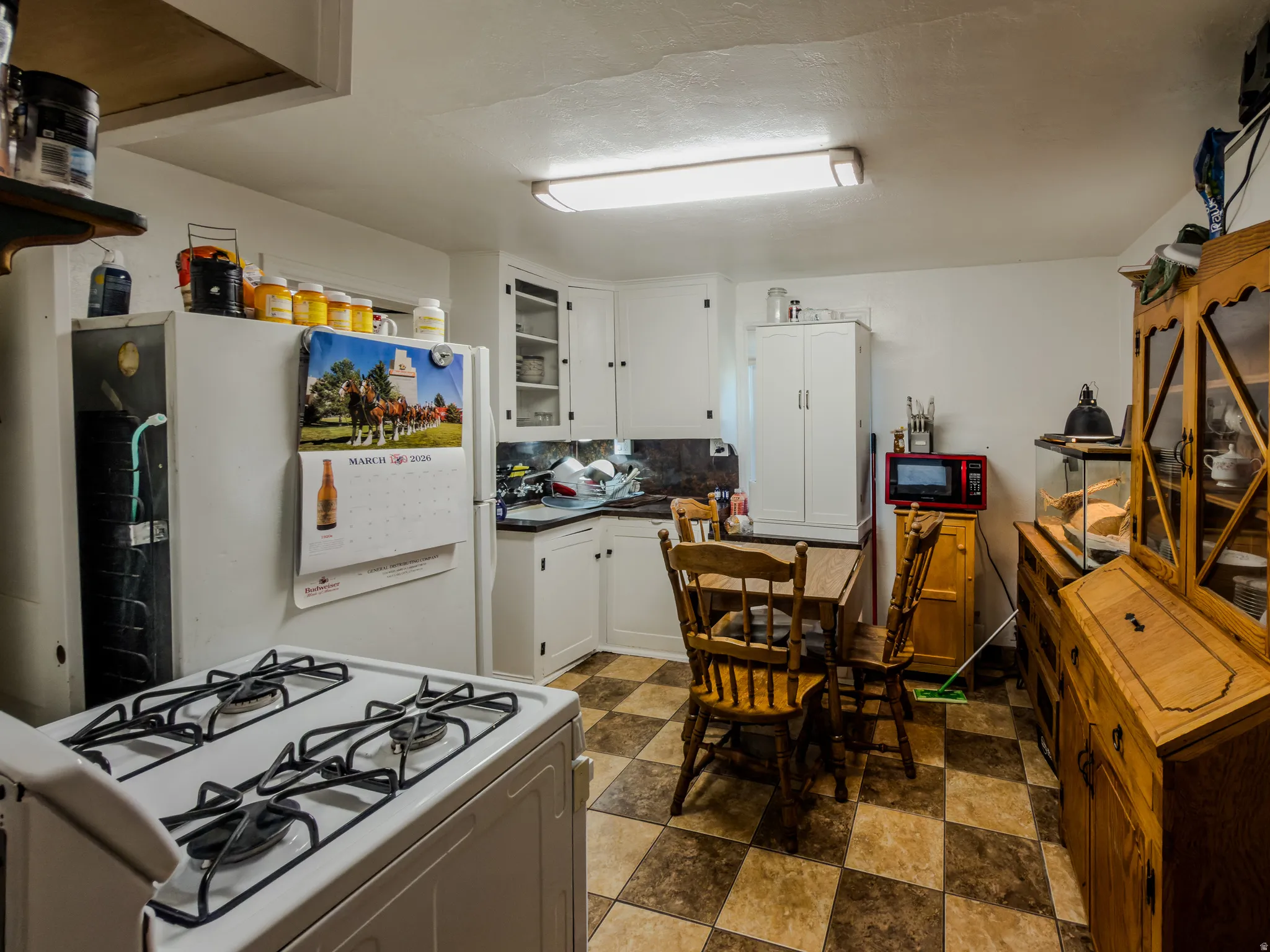 Kitchen featuring white gas range, backsplash, white cabinets, and stone finish flooring