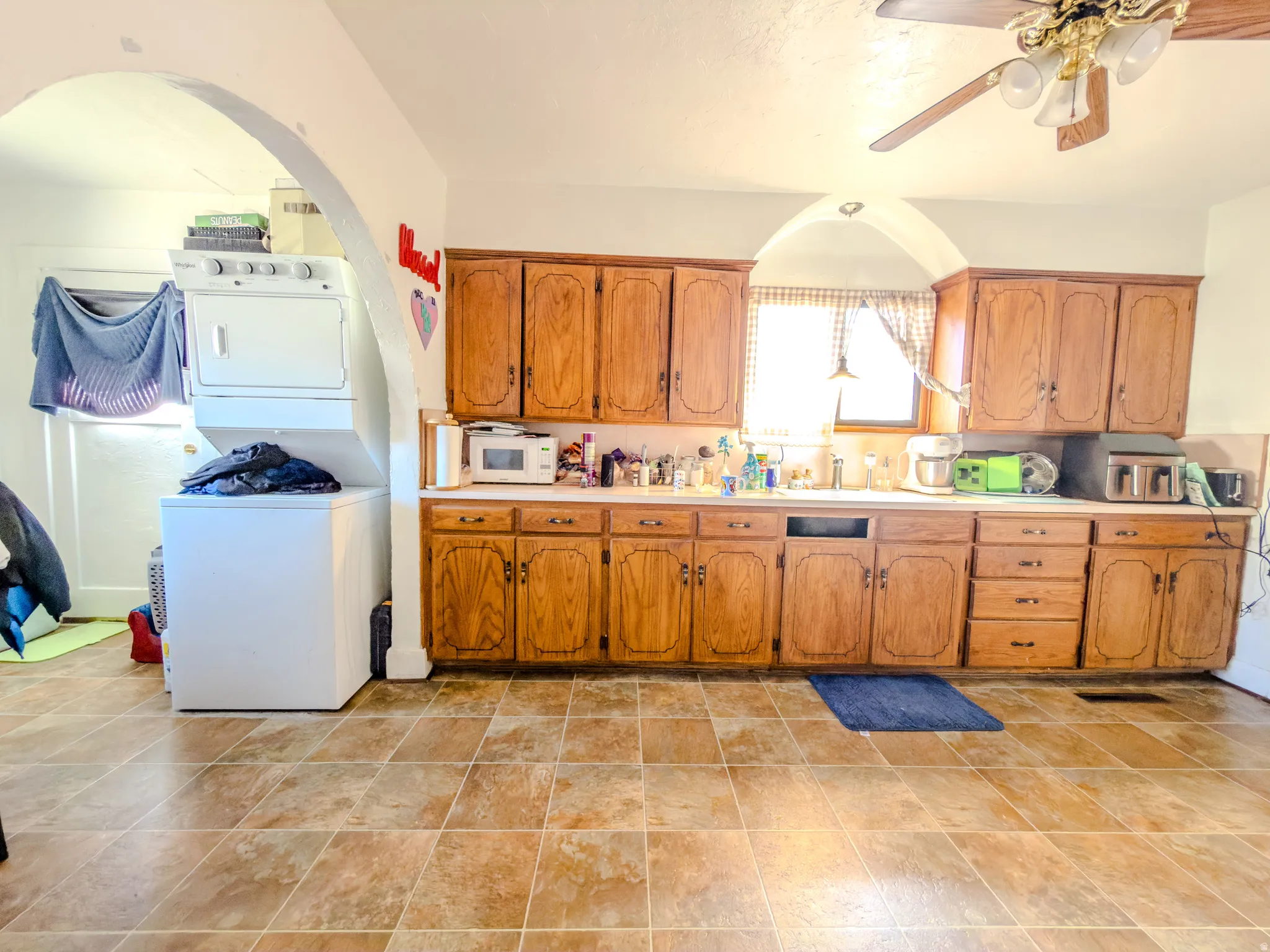 Kitchen featuring light countertops, wood finish cabinets, ceiling fan, stacked washer and dryer, and white microwave