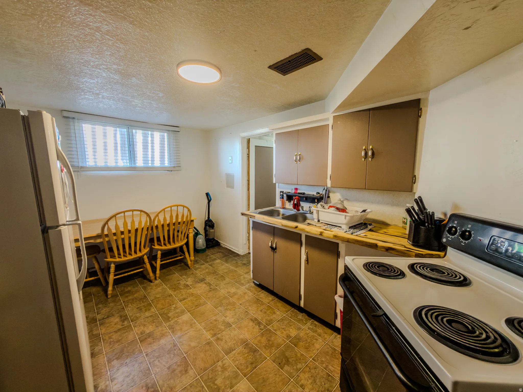 Kitchen with electric range, freestanding refrigerator, a textured ceiling, and light countertops