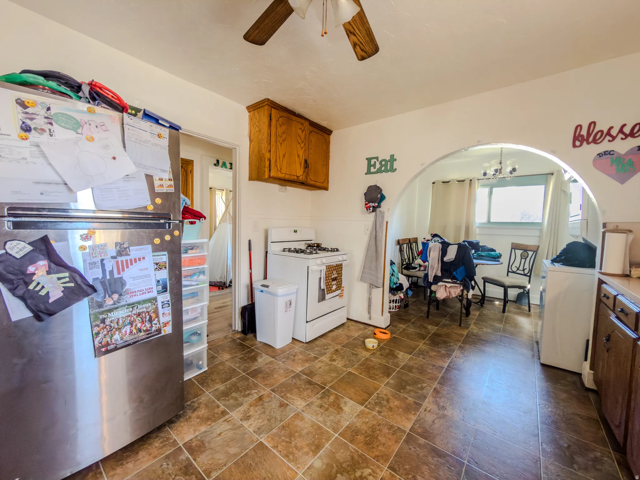 Kitchen featuring freestanding refrigerator, wood finish cabinetry, gas range gas stove, ceiling fan, and arched walkways