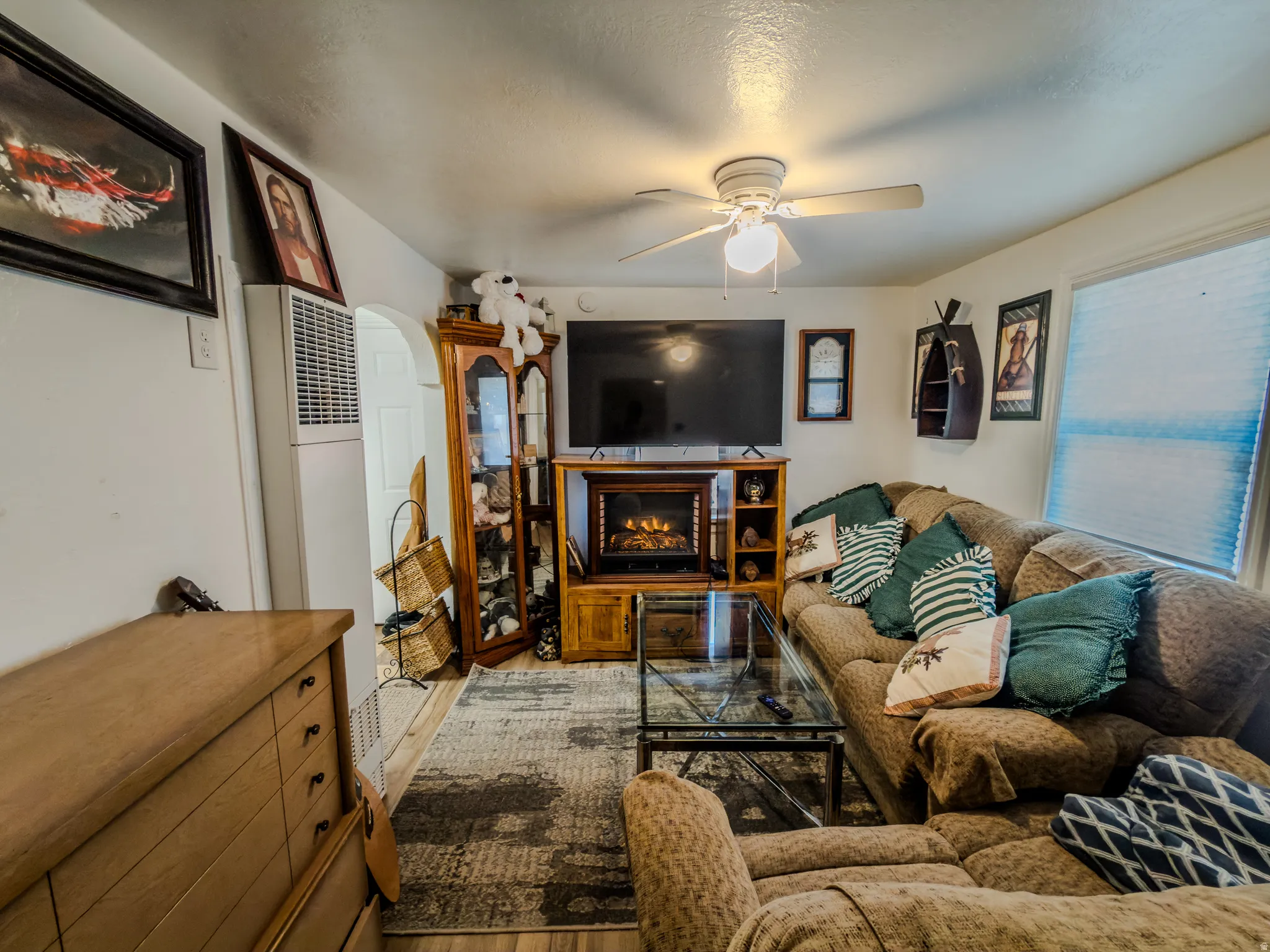 Living room with a heating unit, ceiling fan, wood finished floors, a lit fireplace, and arched walkways
