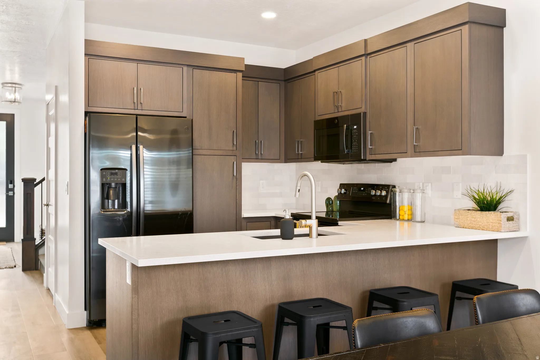 Kitchen featuring a peninsula, black appliances, a kitchen breakfast bar, tasteful backsplash, and light stone countertops