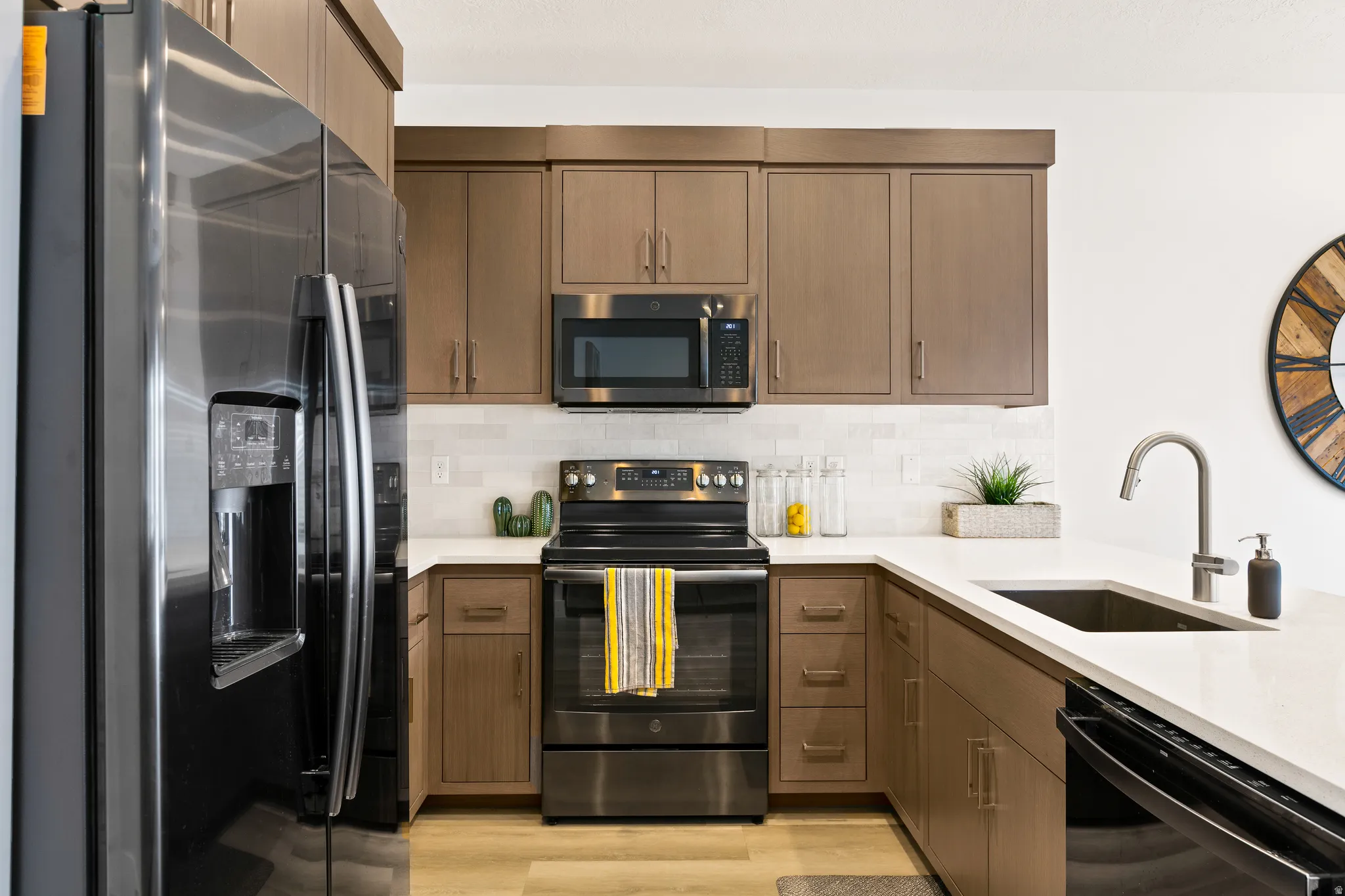 Kitchen with stainless steel appliances, backsplash, light wood finished floors, and light stone countertops
