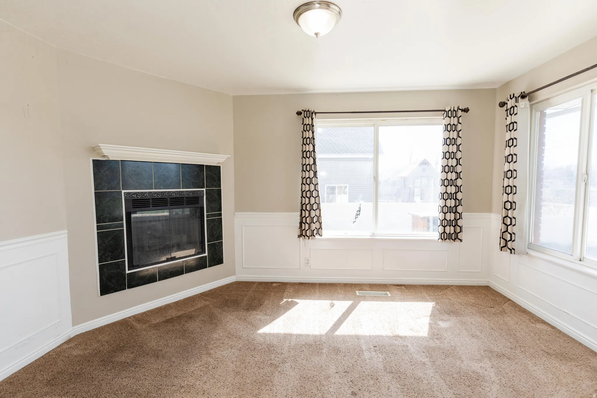 Spare room featuring a decorative wall, wainscoting, a tiled fireplace, and carpet