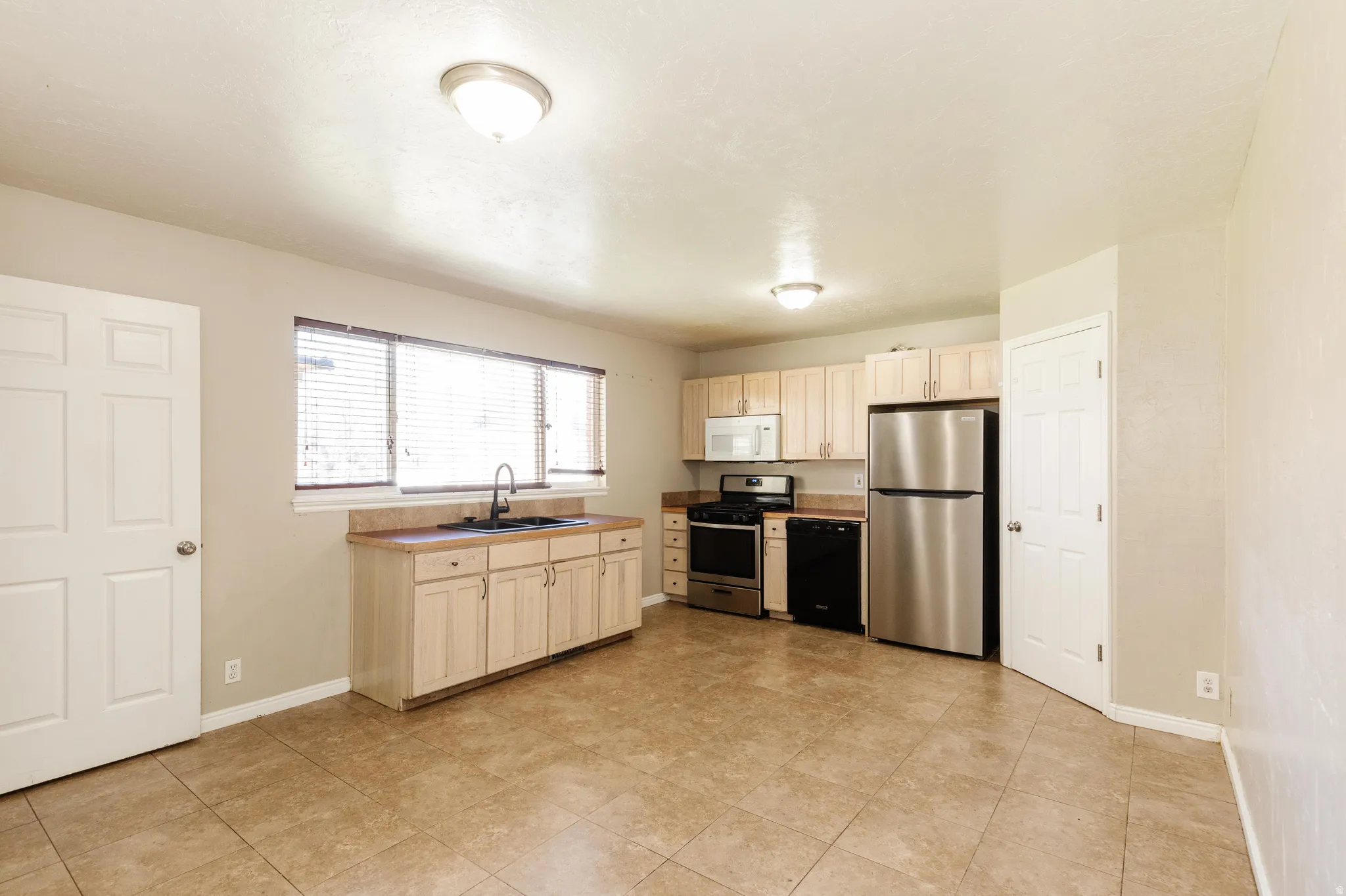 Kitchen with stainless steel appliances, light wood finish cabinetry, light countertops, and light tile patterned floors