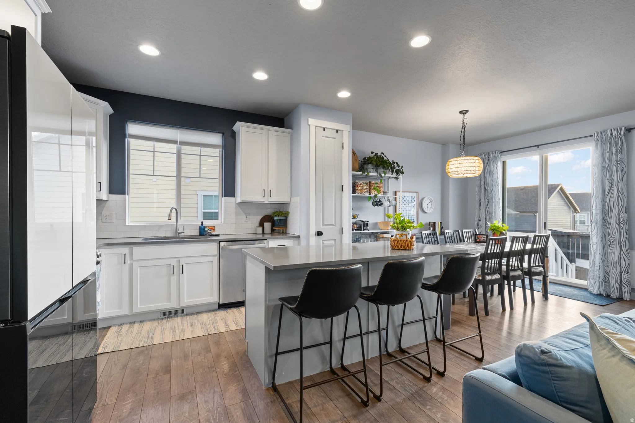 Kitchen with stainless steel appliances, tasteful backsplash, white cabinetry, light wood finished floors, and decorative light fixtures