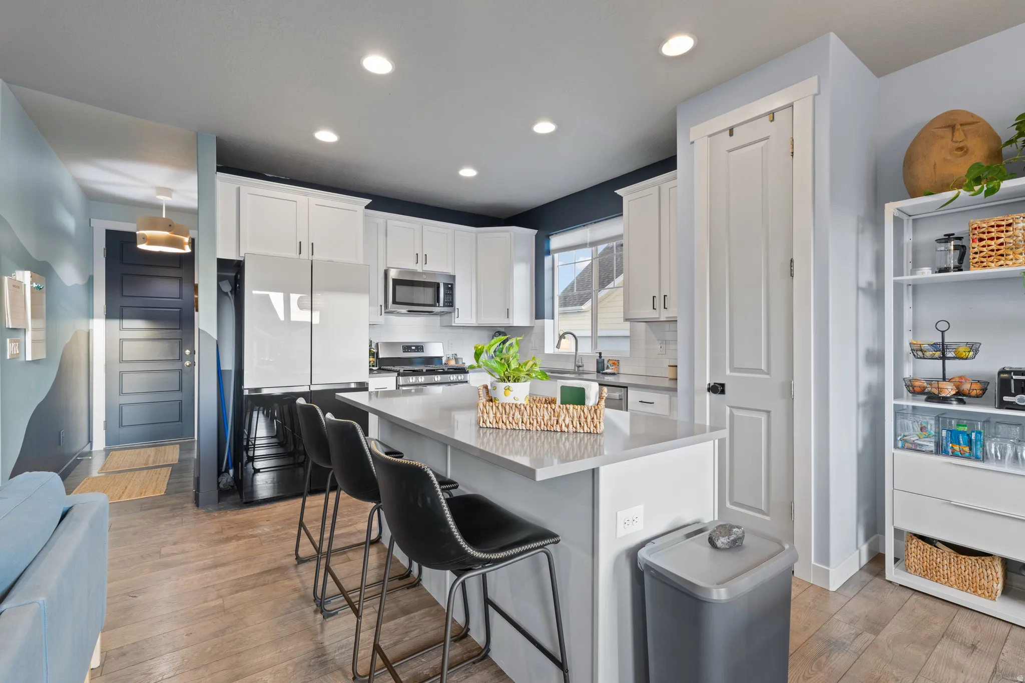 Kitchen with a kitchen island, a kitchen bar, white cabinets, stainless steel appliances, and light wood-style floors