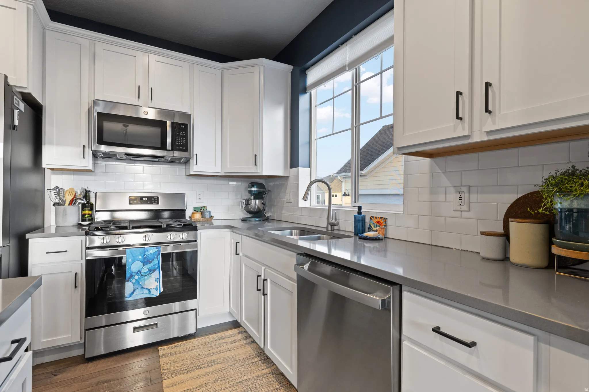 Kitchen with stainless steel appliances, white cabinets, backsplash, dark wood-style flooring, and dark stone countertops